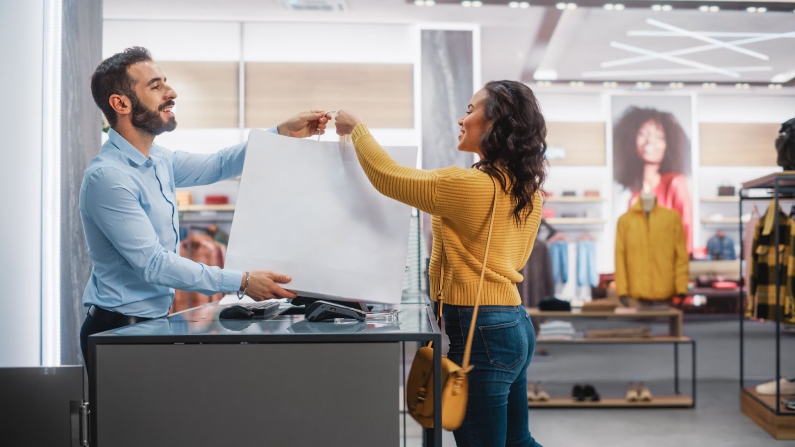 Alt text: A retail sales assistant gives a female customer a shopping bag with new clothes.