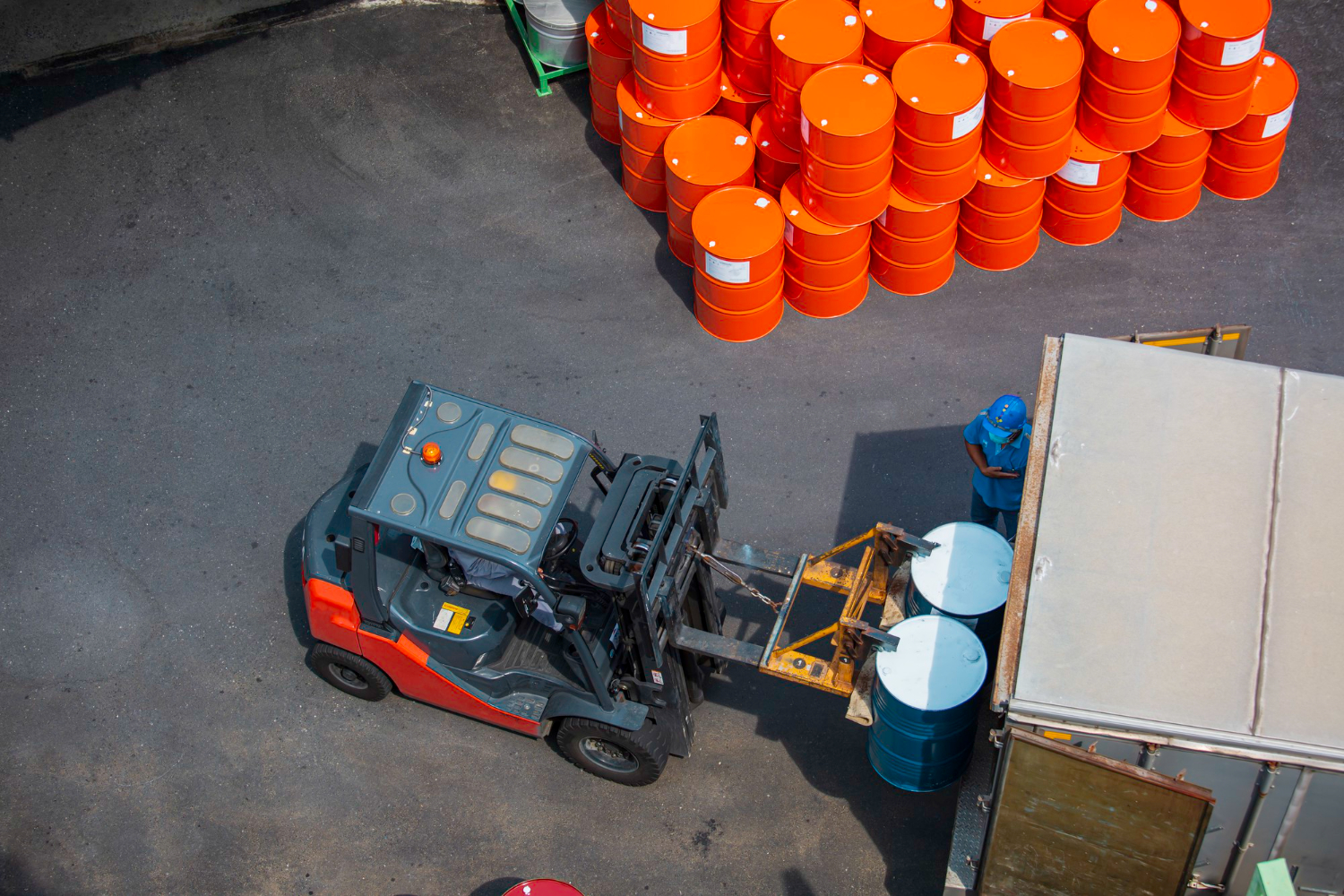 Alt text: Top view of oil barrels being carried by a forklift truck onto a truck.