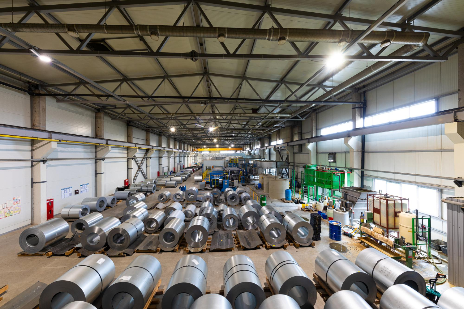 Alt text: Rolls of steel sheets are stored inside a giant warehouse.