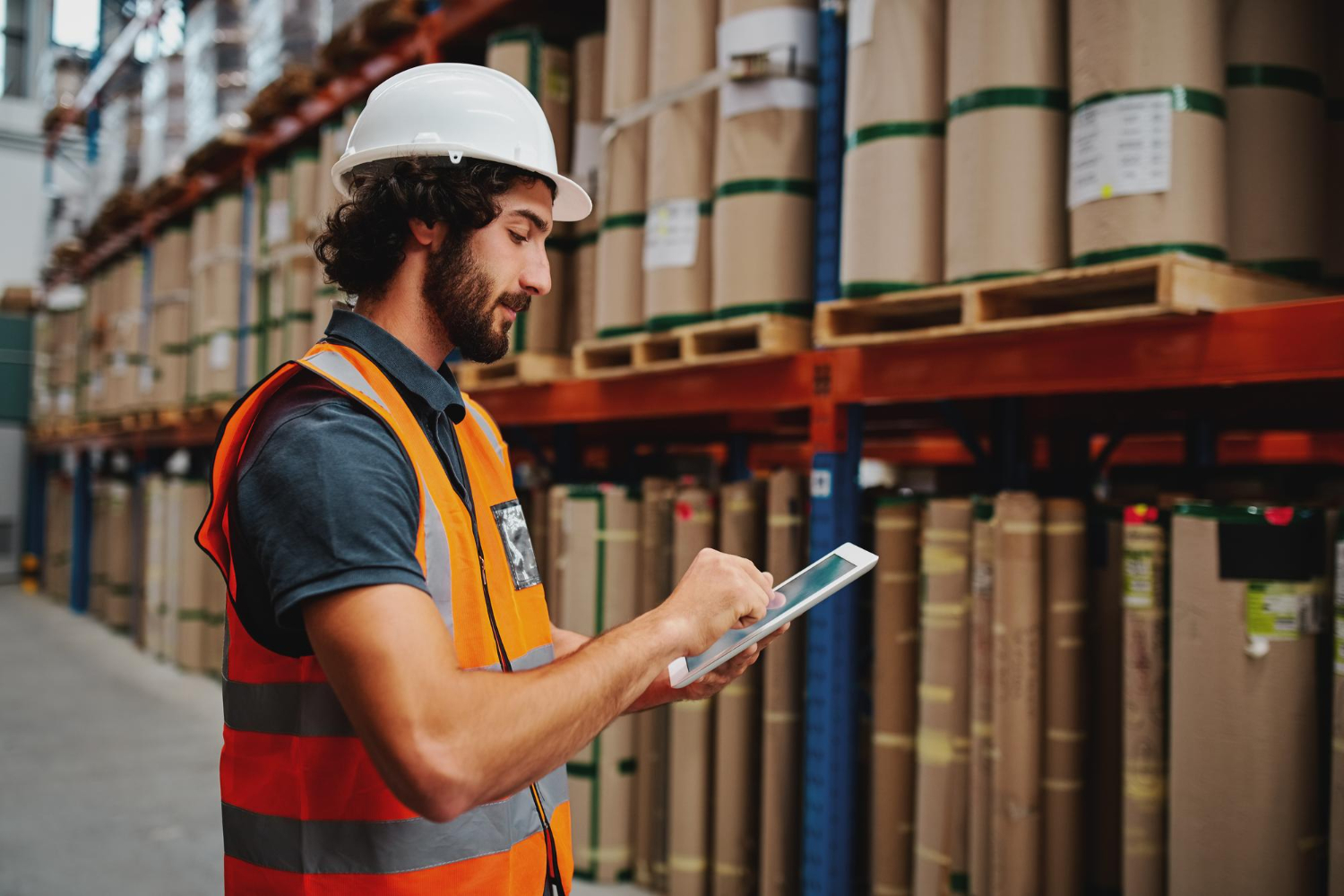 Alt text: A man with a tablet is checking packages in a warehouse.