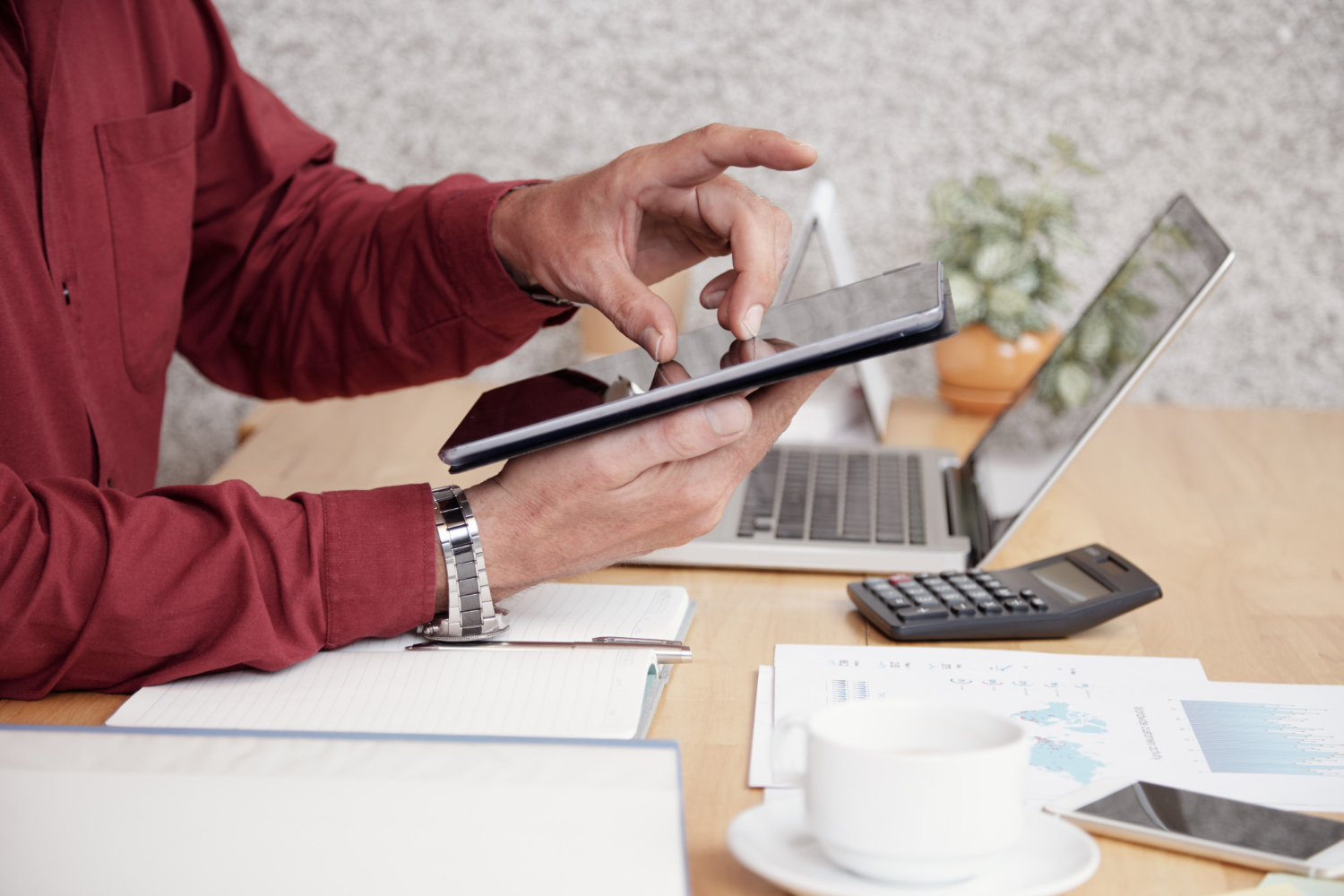 Alt text: Australian business owner using a tablet to calculate import duties and GST, with laptop, calculator, and shipping cost documents on desk.