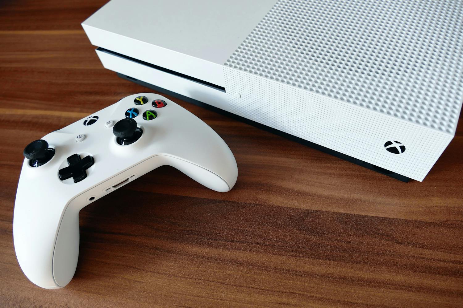 Alt text: White Xbox console with controller on a wooden table.