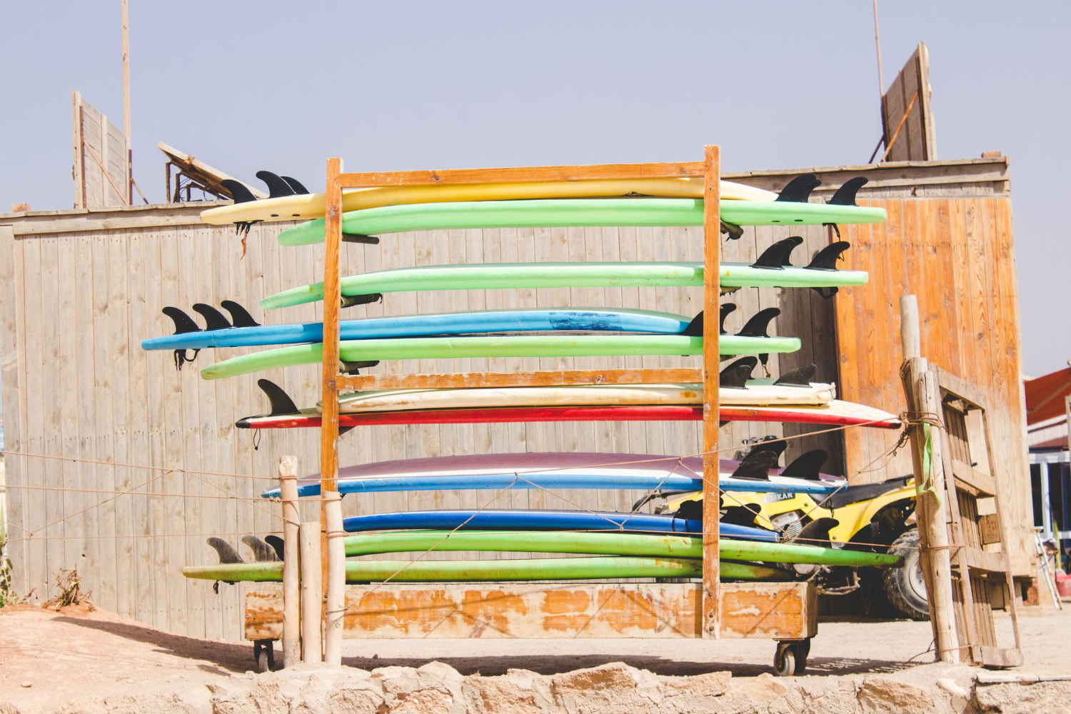 Alt text: Rack of colourful surfboards stacked vertically outside a wooden beach shack.