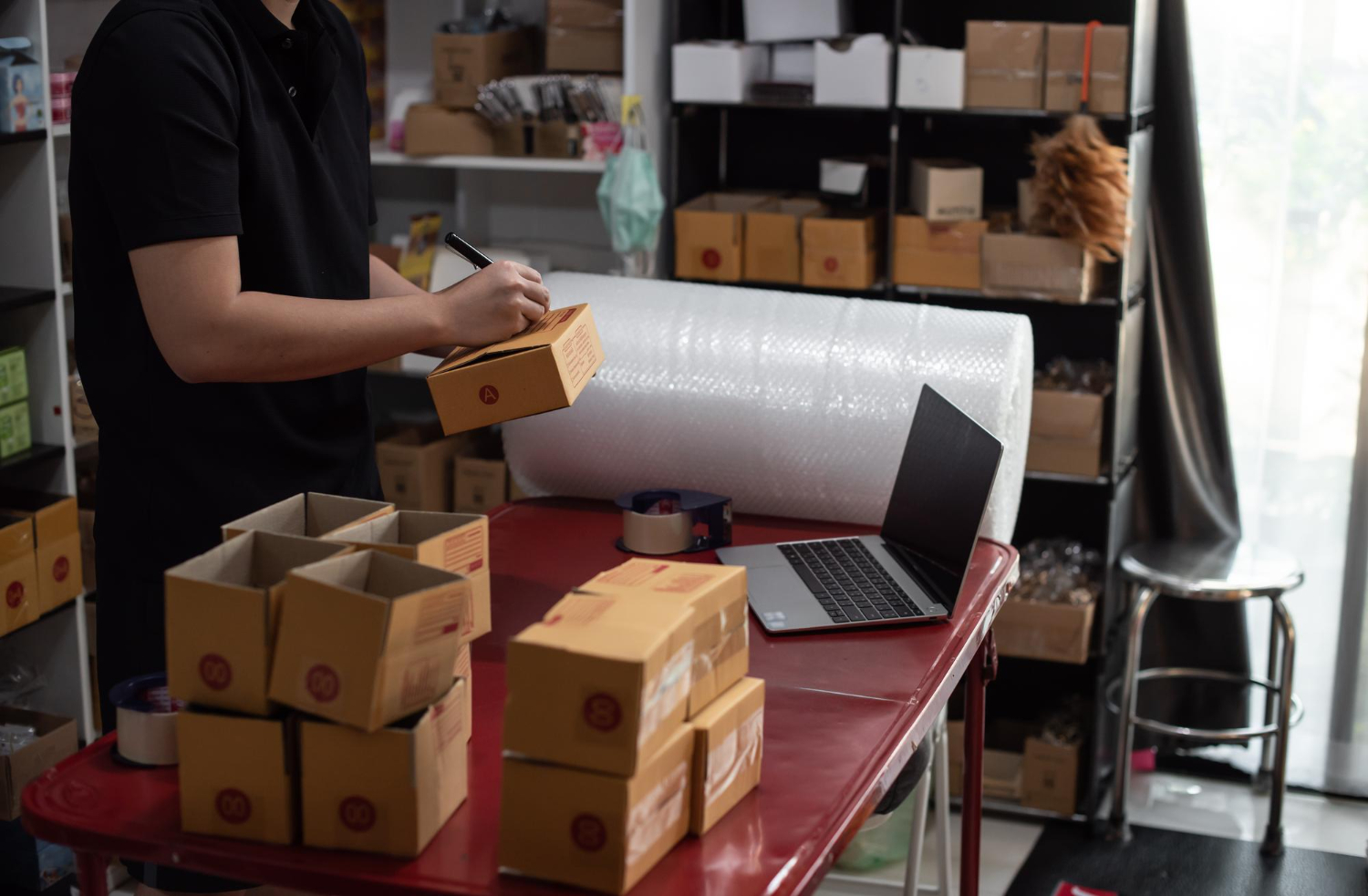 Alt text: A person is writing on a packaging box while standing in front of a table with packaging supplies.