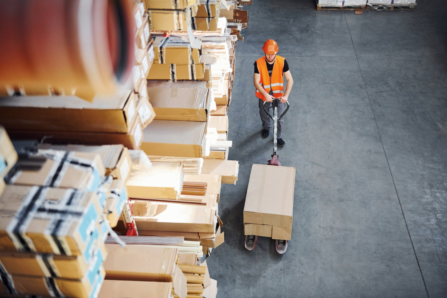 Alt text: Warehouse staff moving a large box with a pallet jack among stacked packages.