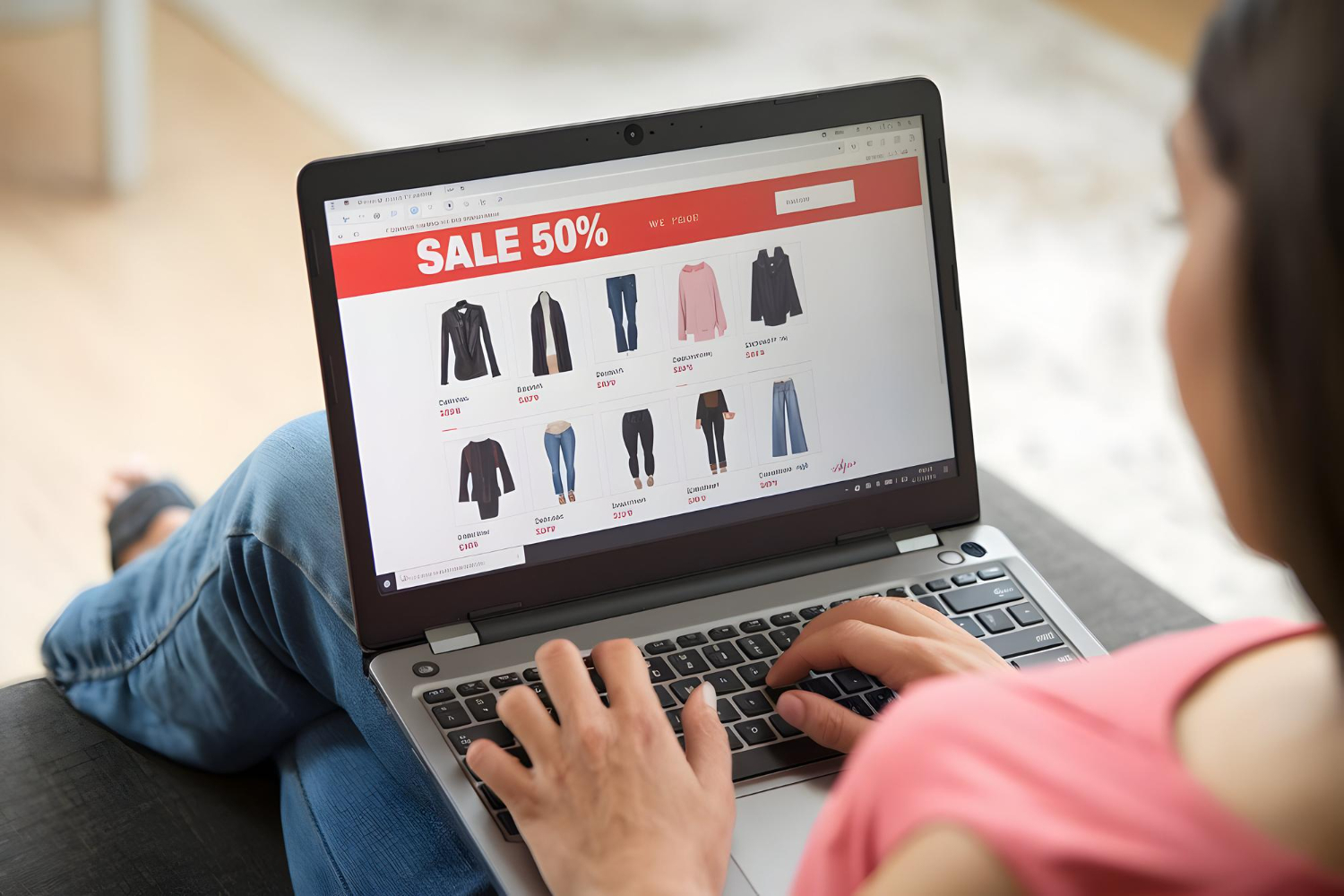Alt text: A woman is her laptop, looking at an e-commerce website that is selling clothing apparel. A banner saying “sale 50%” can be seen at the top of the webpage.