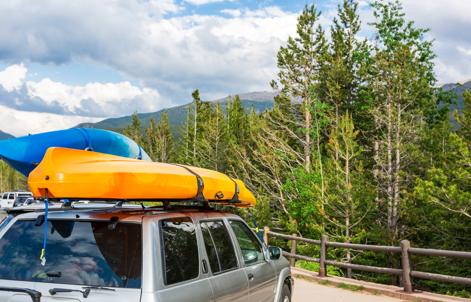 Alt text: A car with two kayaks strapped to its roof rack is parked near a forest.