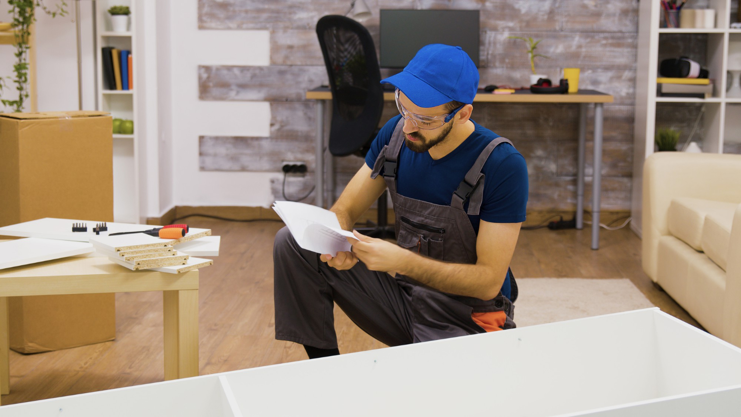 Alt text: A male delivery worker, wearing protective glasses, is setting up a piece of furniture in an apartment.