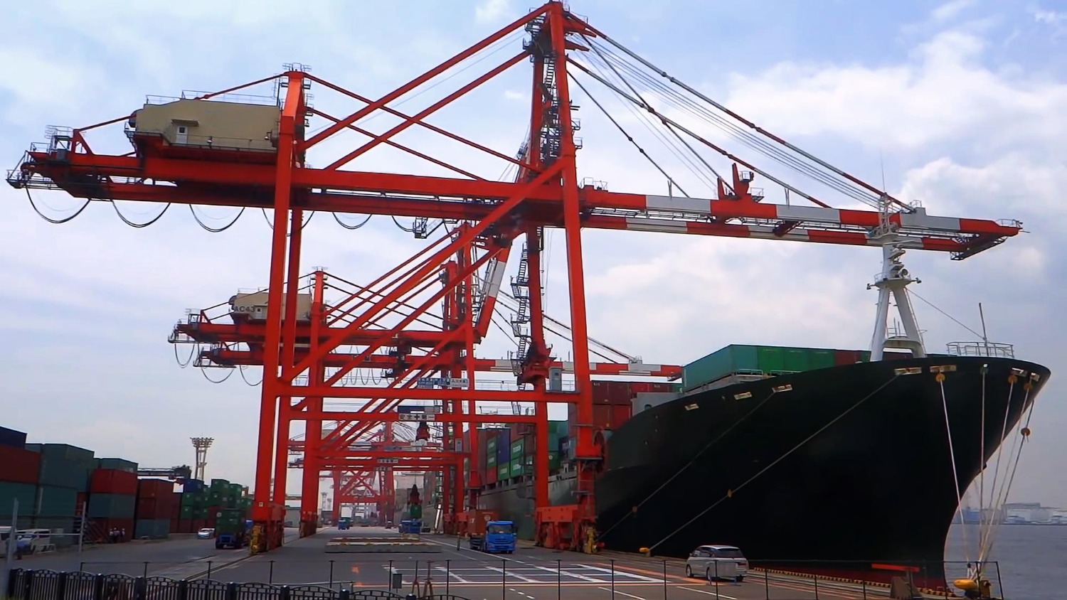 Alt text: A large container ship rests at the port, surrounded by cranes and stacks of cargo containers