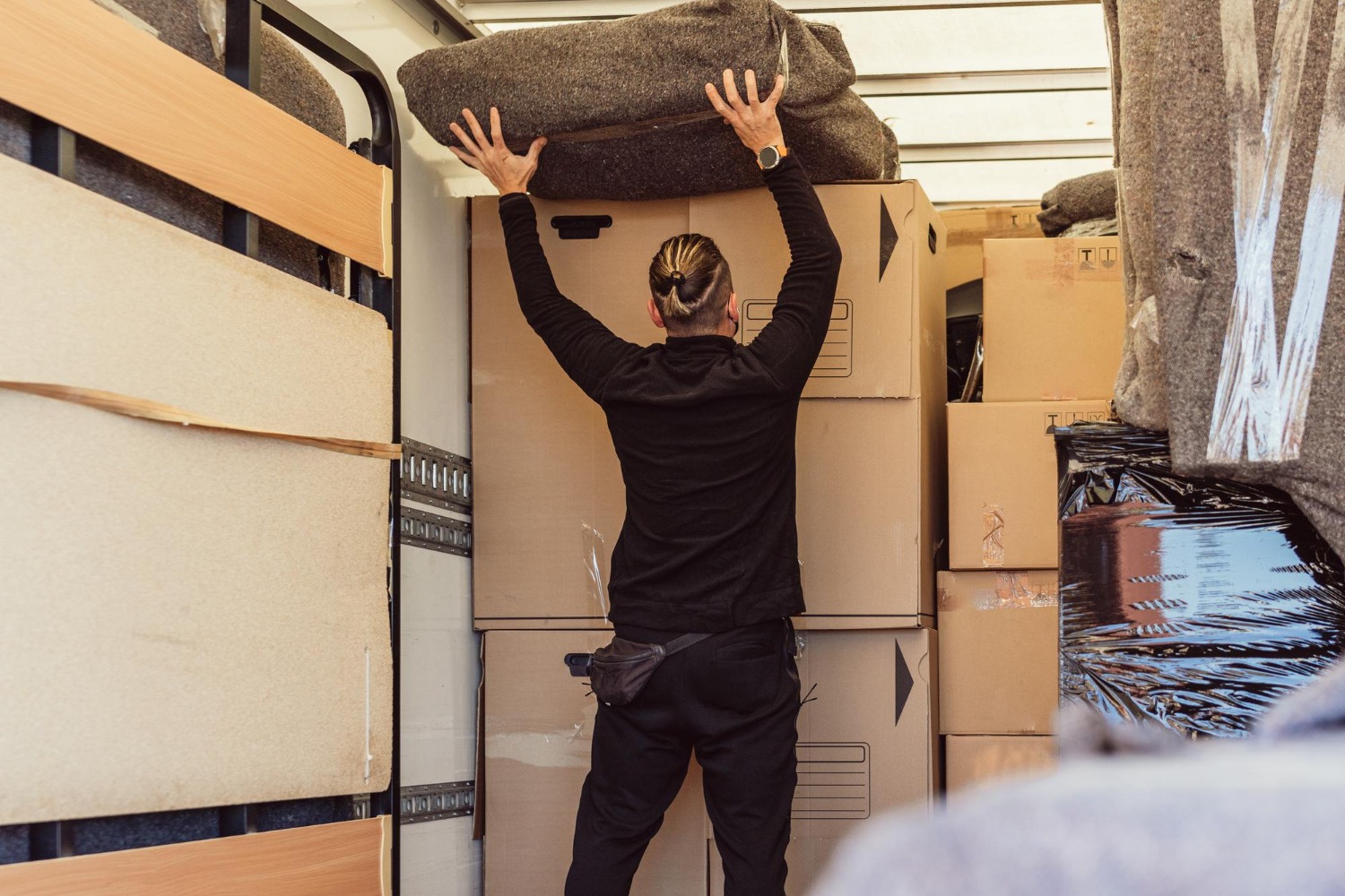 Alt text: A man lifts a large furniture into a moving truck during a busy moving day.