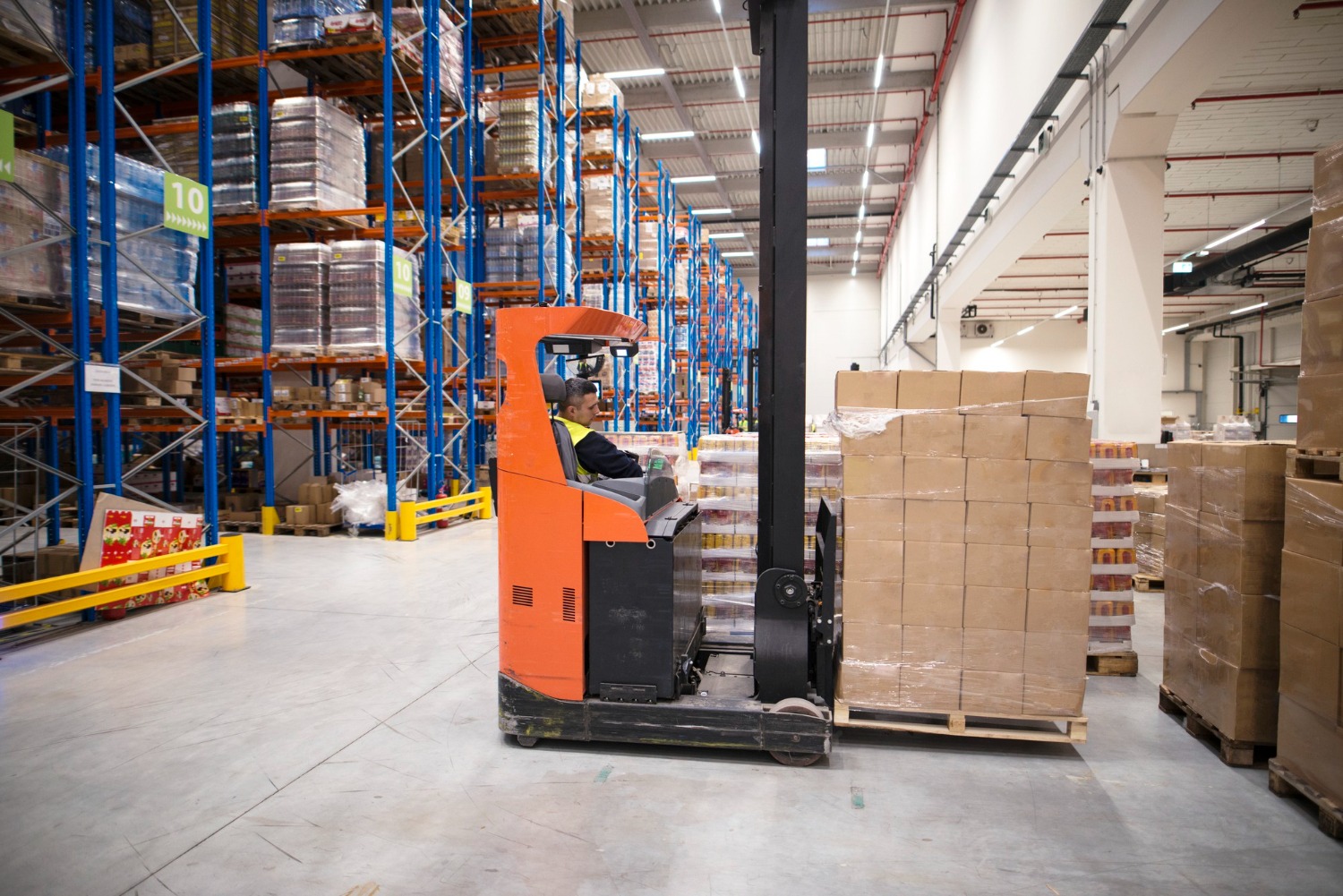 Alt text: Industrial worker in protective uniform operating a forklift in a warehouse distribution centre.