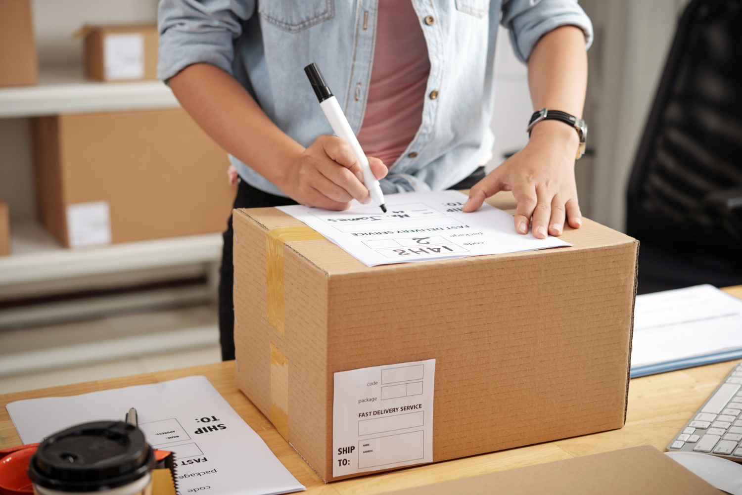 Alt text: Person labelling a cardboard box with a packing slip in a small business workspace, preparing an order for shipping.