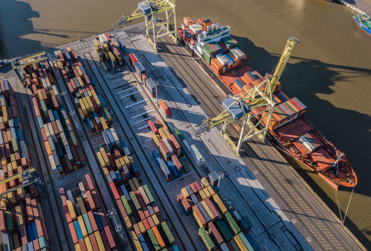 Alt text: An aerial shot of a shipping port with a container ship being loaded.