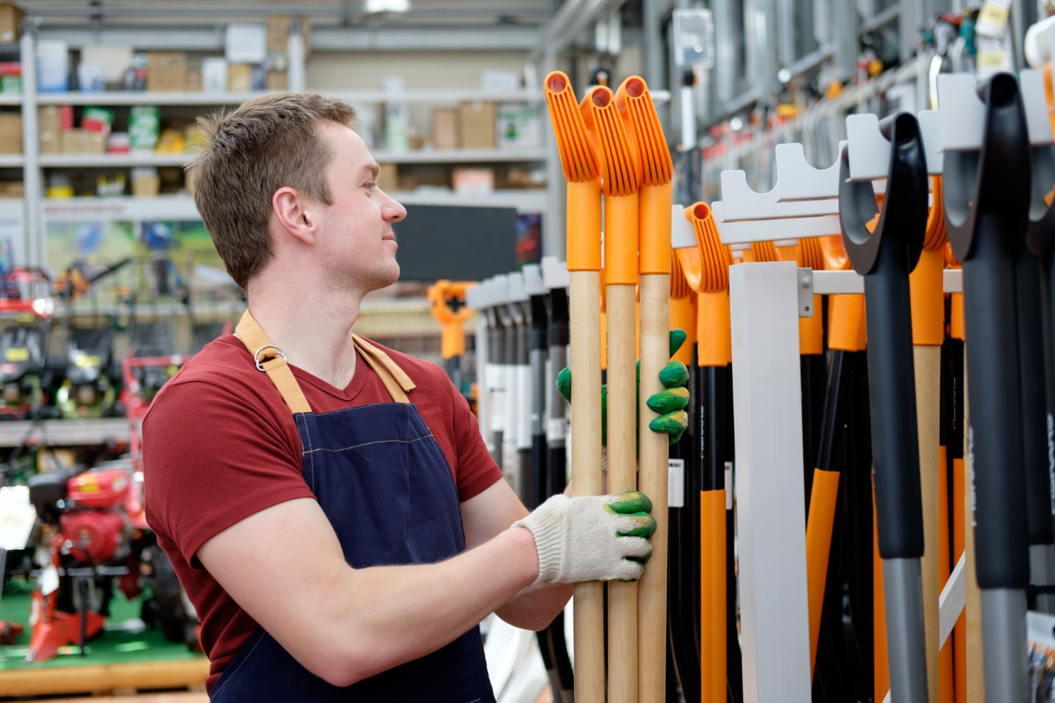 Alt text: A store worker arranging garden tools at a Bunnings-style hardware warehouse.