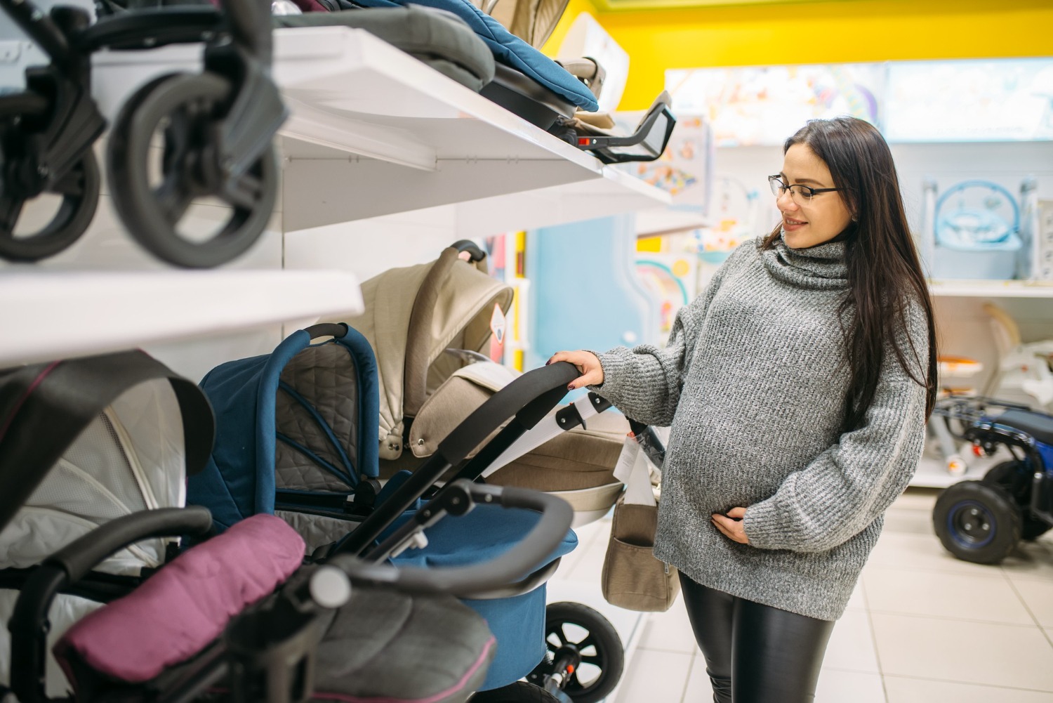 Alt text: A pregnant woman is looking through strollers in a shop.