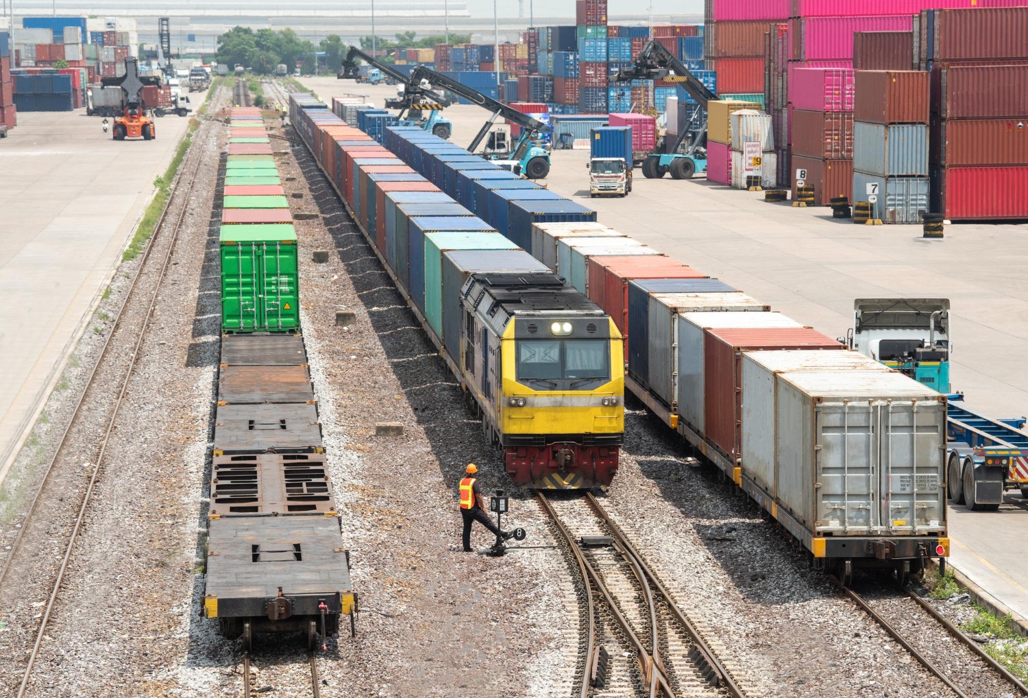 Alt text: Freight trains are being loaded with container units at a shipping depot.