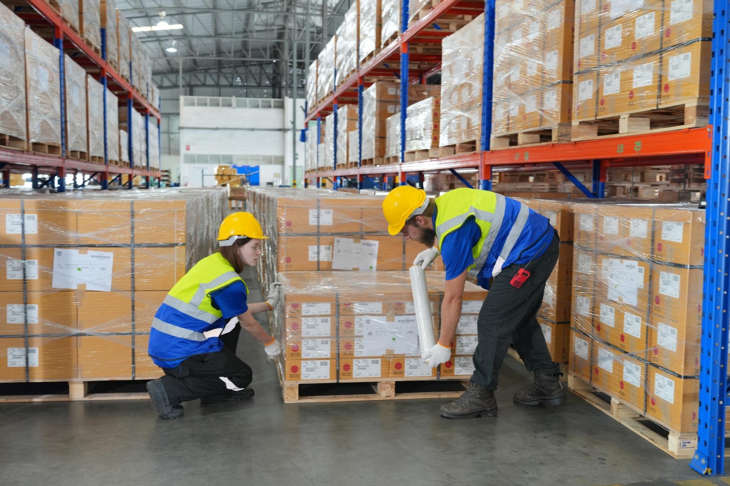 Alt text: Two warehouse workers are securing a pallet with a plastic.