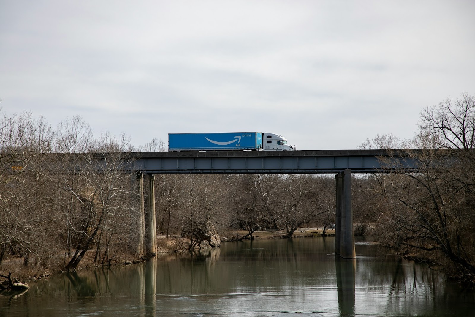 Alt text: An Amazon truck is driving on a bridge over a river.