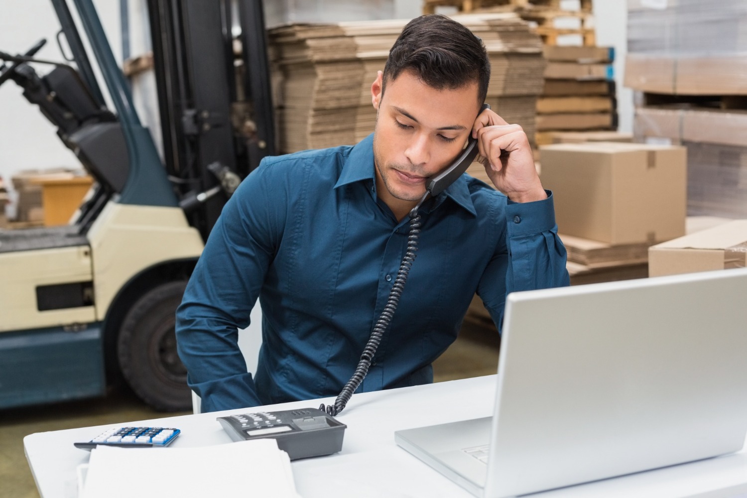 Alt text: Warehouse manager uses their telephone and laptop.