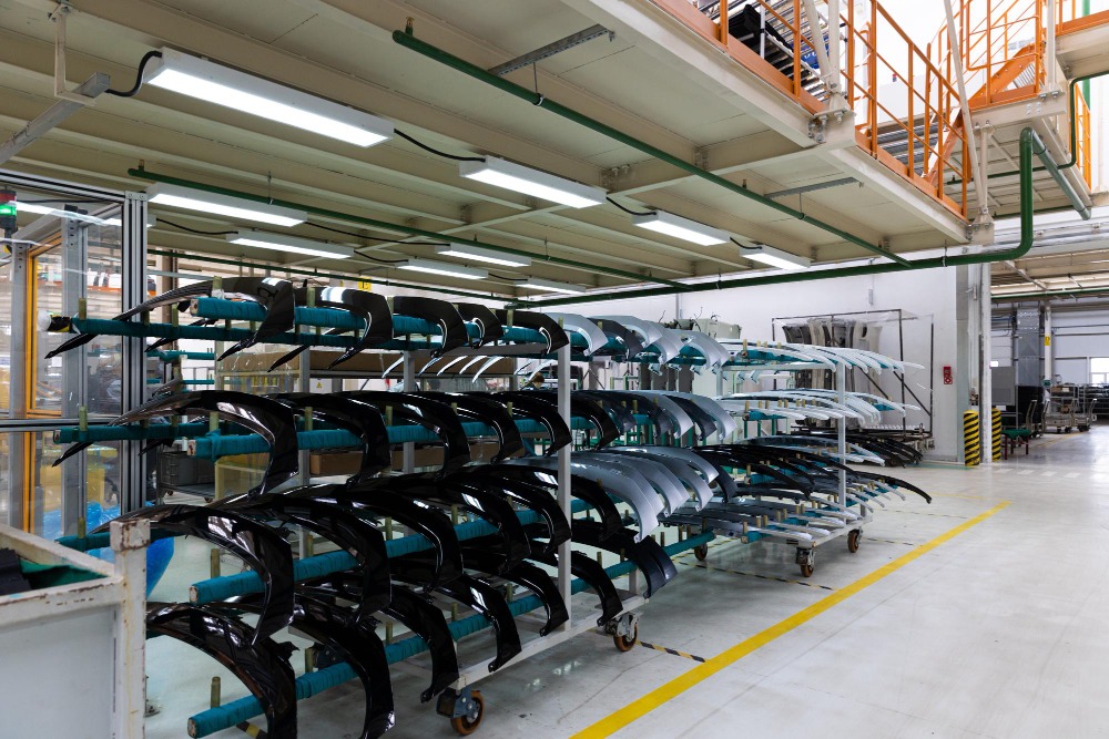 Alt text: Rows of glossy black and gray curved automotive body panels are neatly stored on wheeled metal rack.