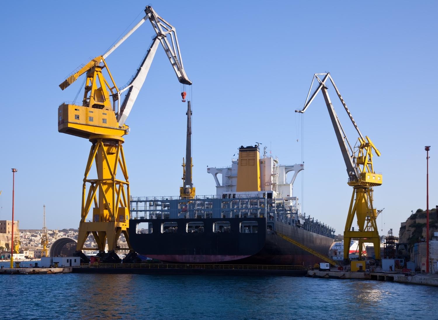 Alt text: A container ship is docked at a shipyard.