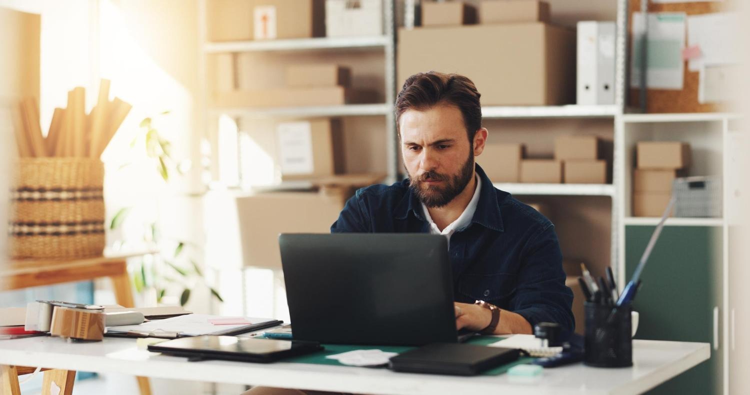 Alt text: A male business owner uses his laptop in his office.
