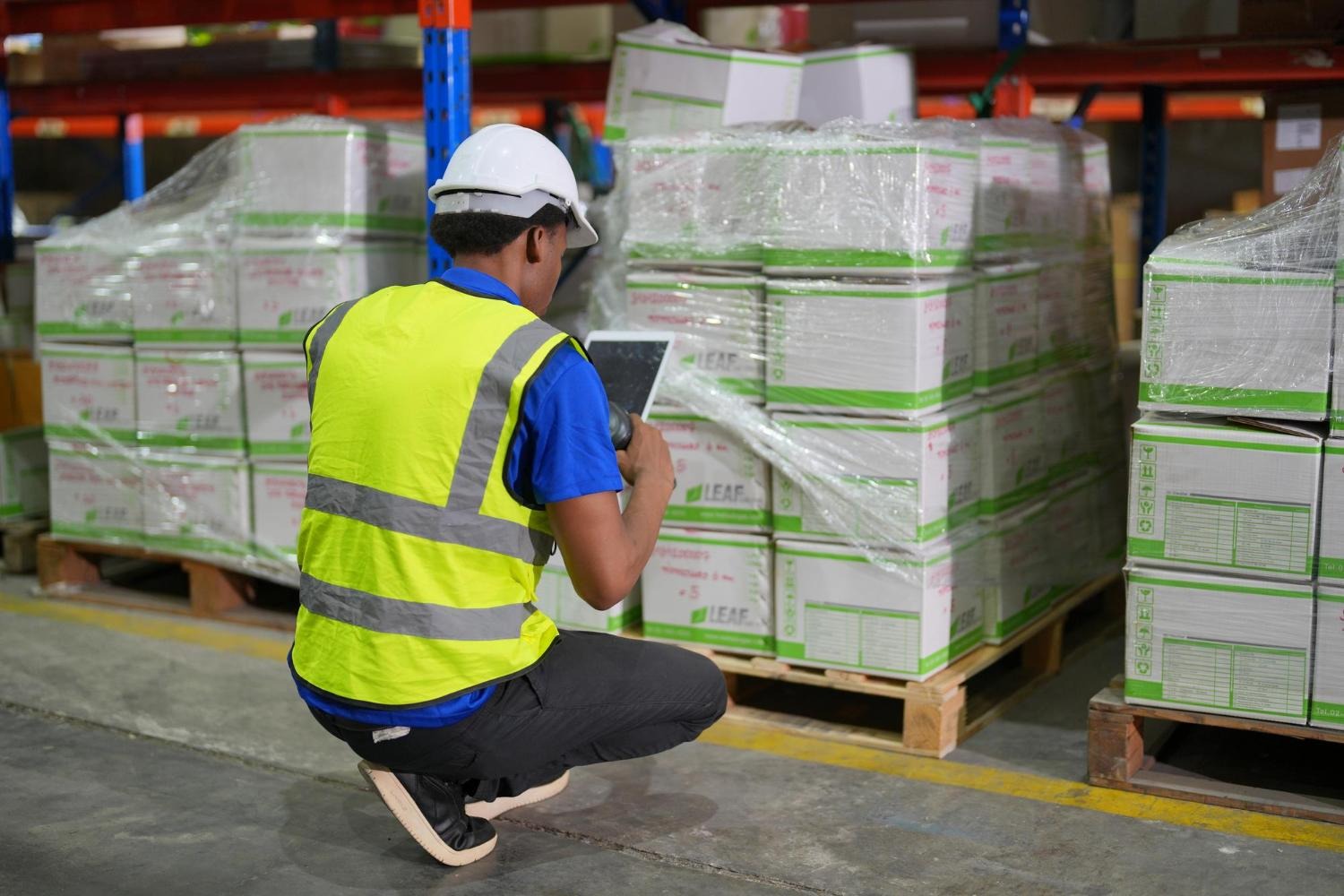 Alt text: A warehouse worker is checking a palletised shipment through a tablet.