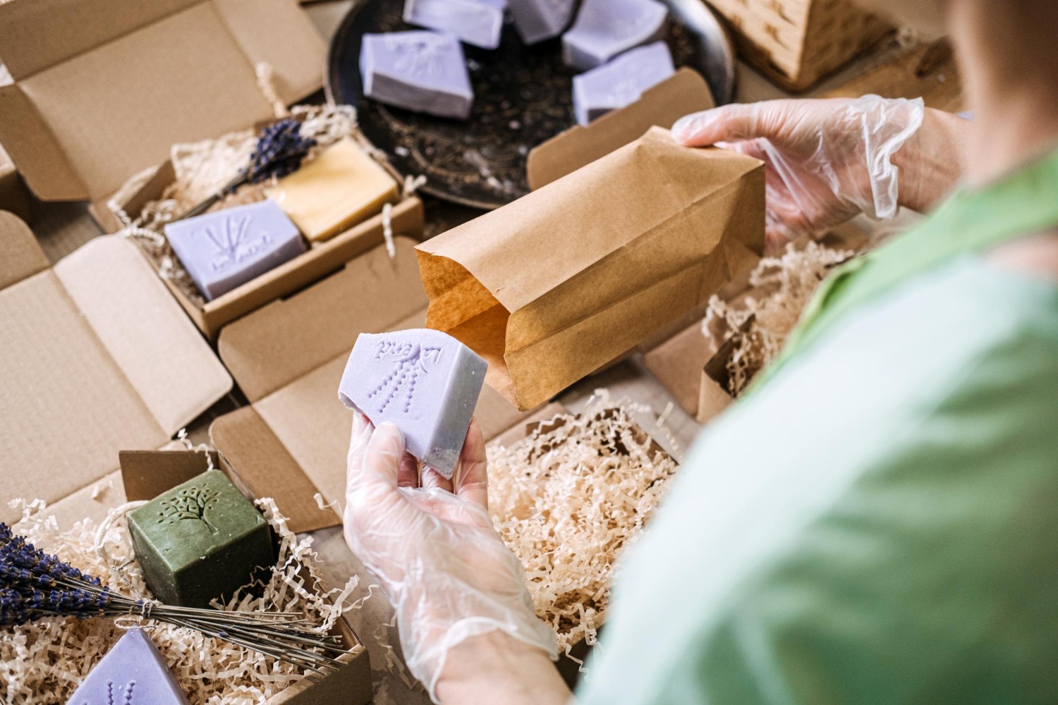 Alt text: Small business owner packing handmade soap bars into recycled cardboard boxes with shredded paper filler and kraft paper bags for eco-friendly shipping.