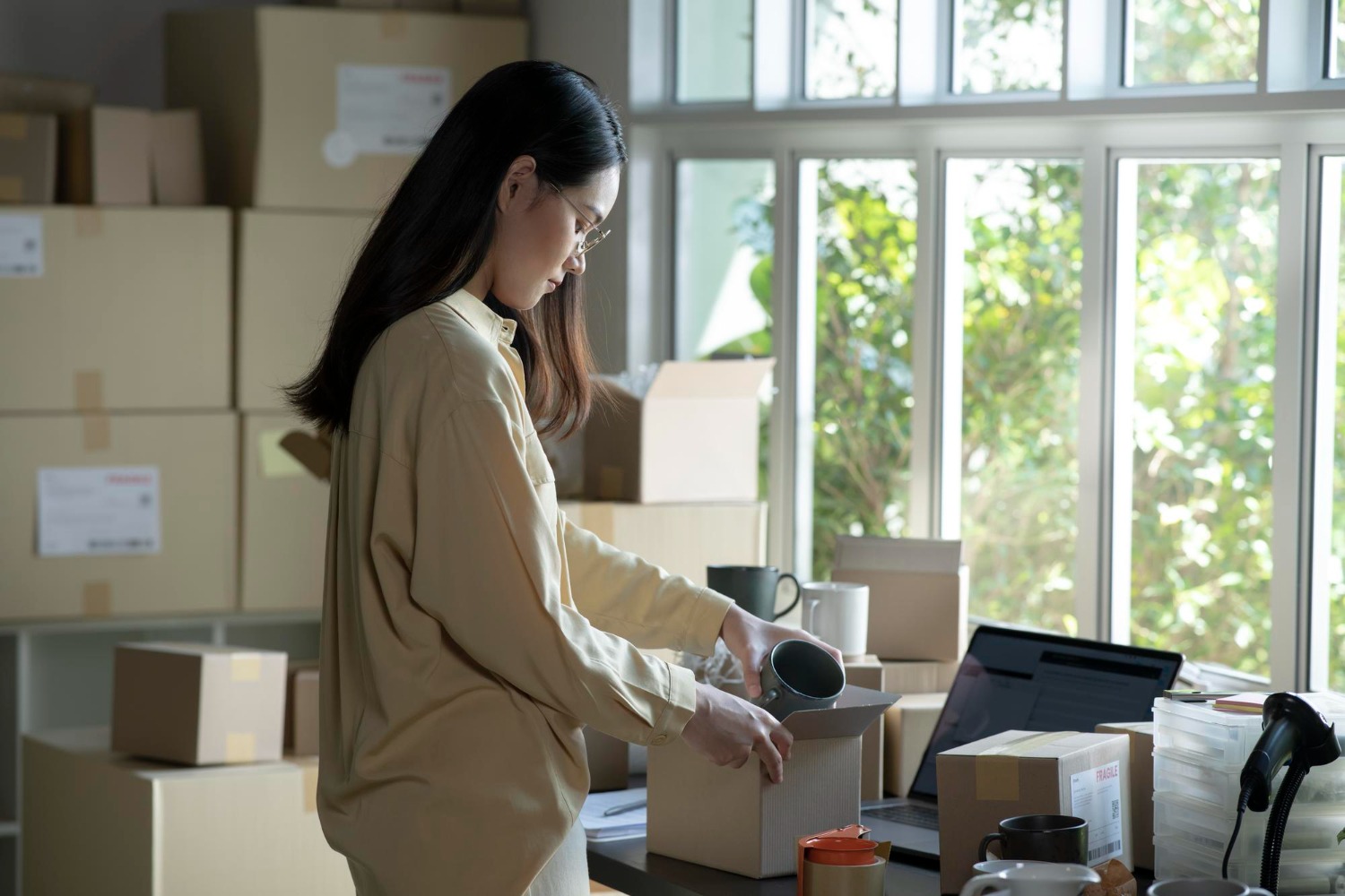 Alt text: Small business owner packing products into shipping boxes at a home workspace before sending inventory to fulfilment centres.