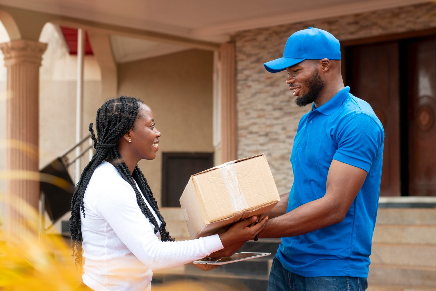 Alt text: Courier handing a parcel to a customer at the front door of a house.