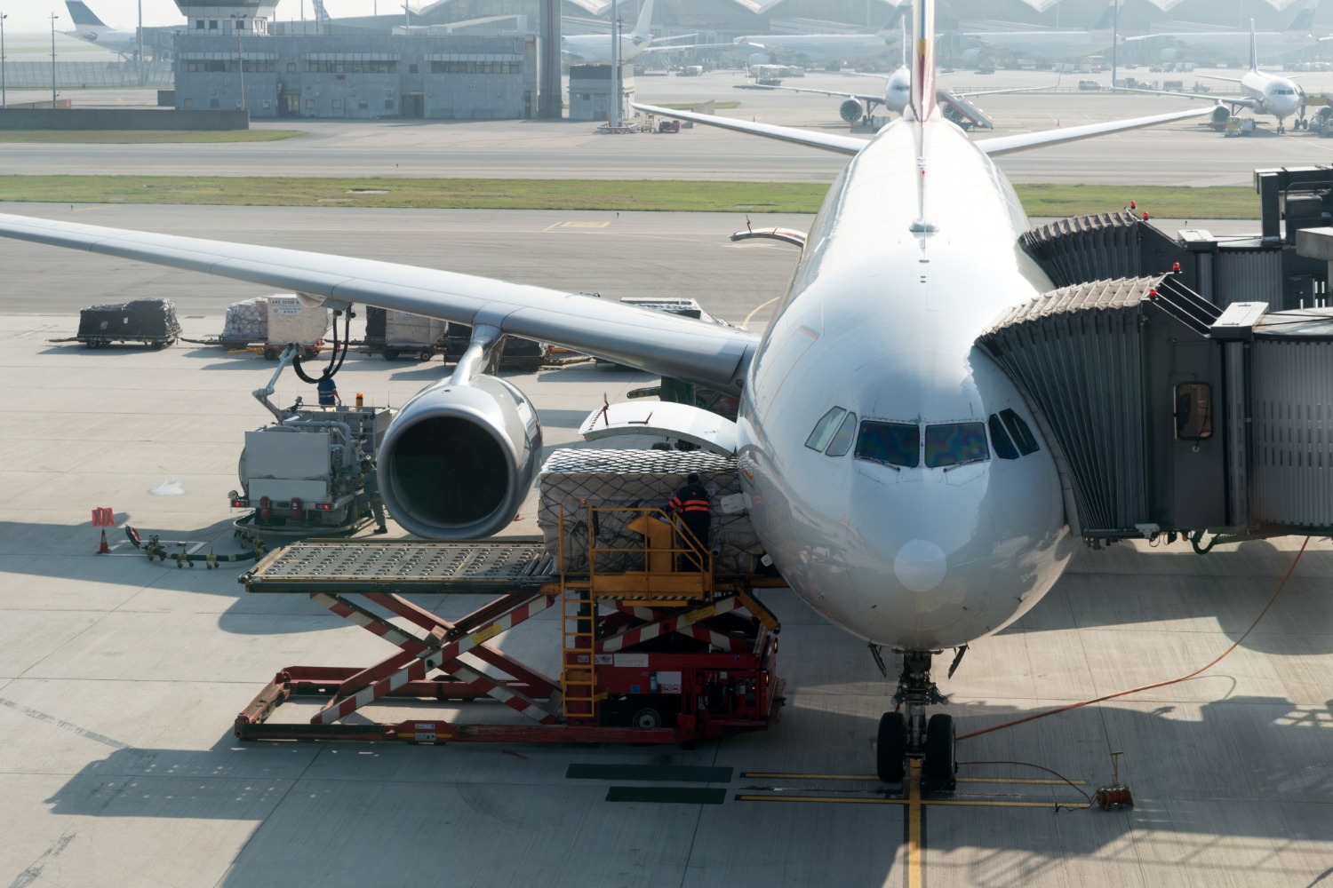 Alt text: Air cargo being loaded onto a commercial aircraft at an airport, with ground crew transferring palletised freight via a cargo lift next to the plane’s fuselage.