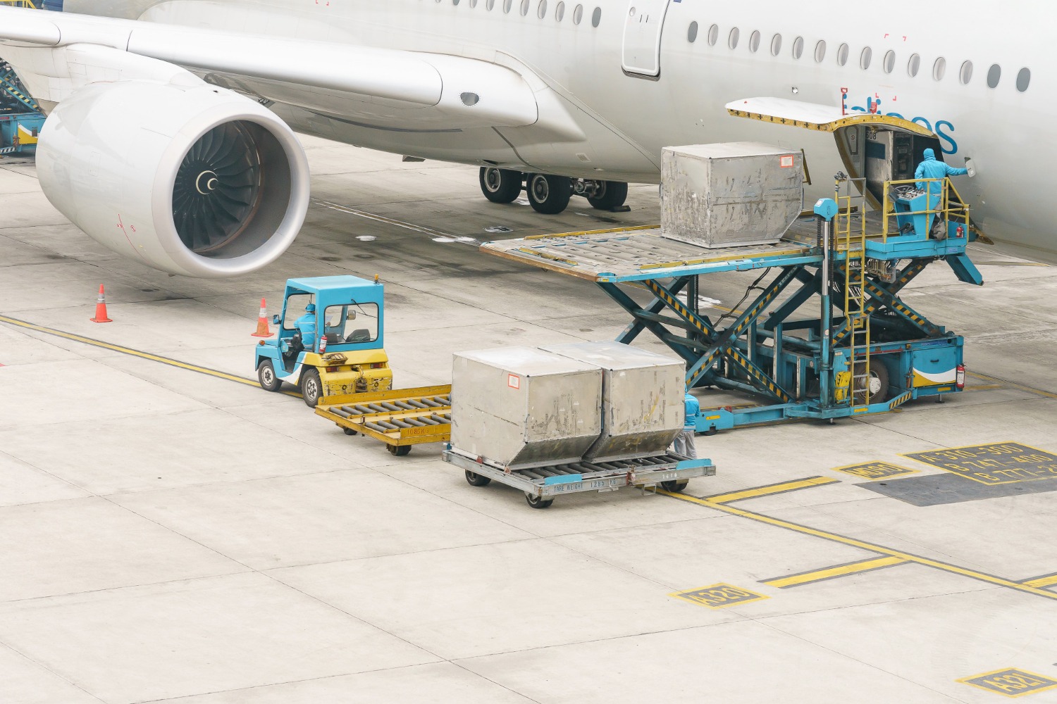 Alt text: Air cargo loading operation at an airport, with ground crew using a hydraulic lift and cargo carts to load freight containers into a commercial aircraft.