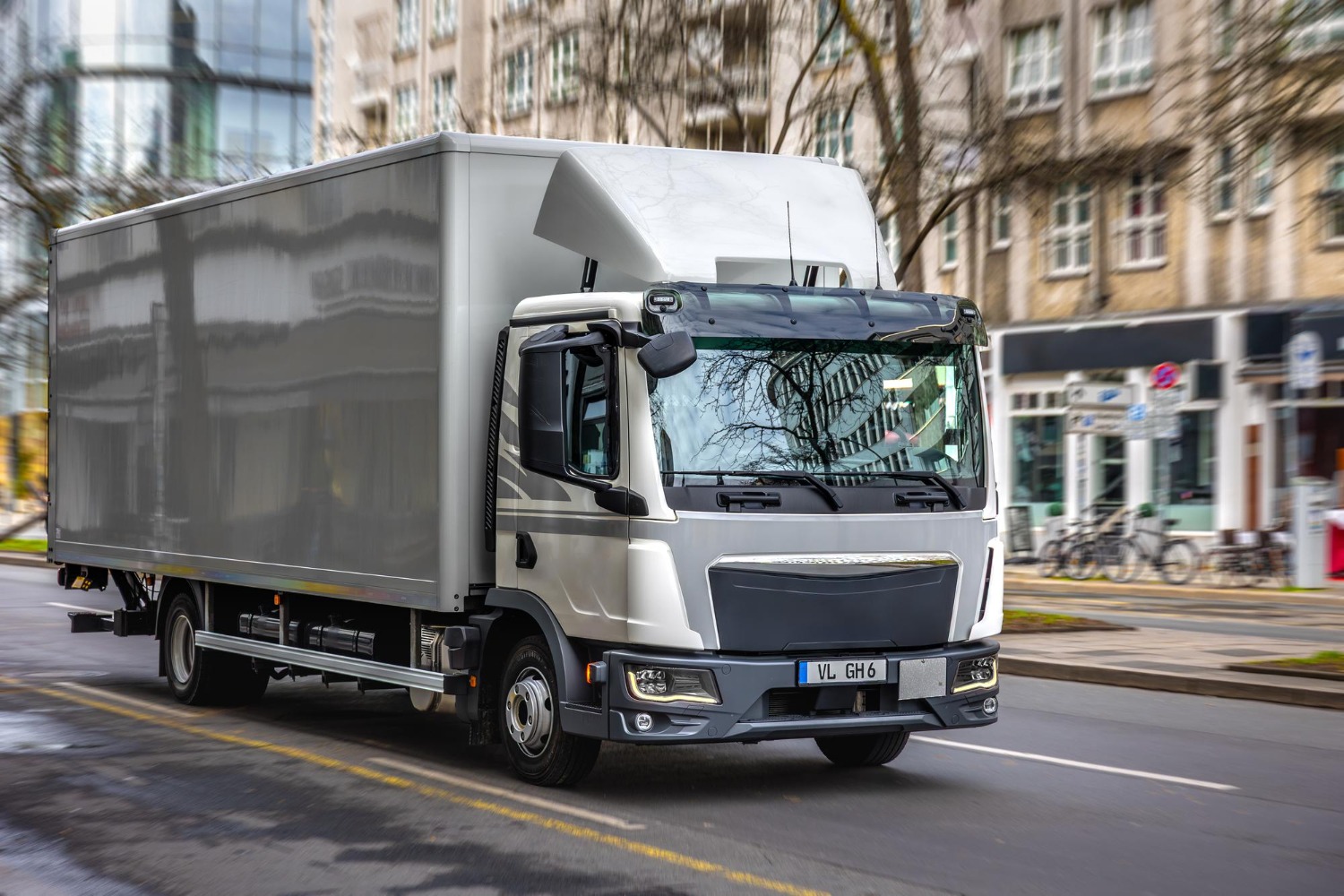Alt text: White box taxi truck driving through an urban street with commercial buildings in the background.