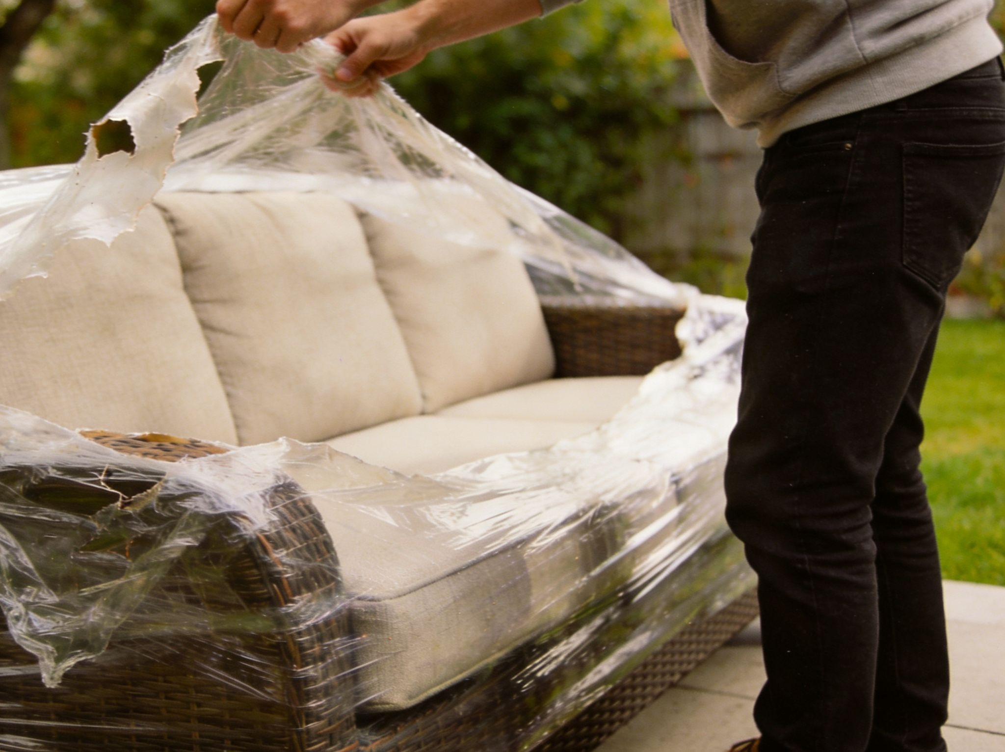 Alt text: Person removing plastic wrap from an outdoor sofa on a patio.