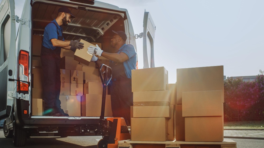 Alt text: Logistics warehouse workers use a hand pallet truck to start loading the delivery truck with cardboard boxes