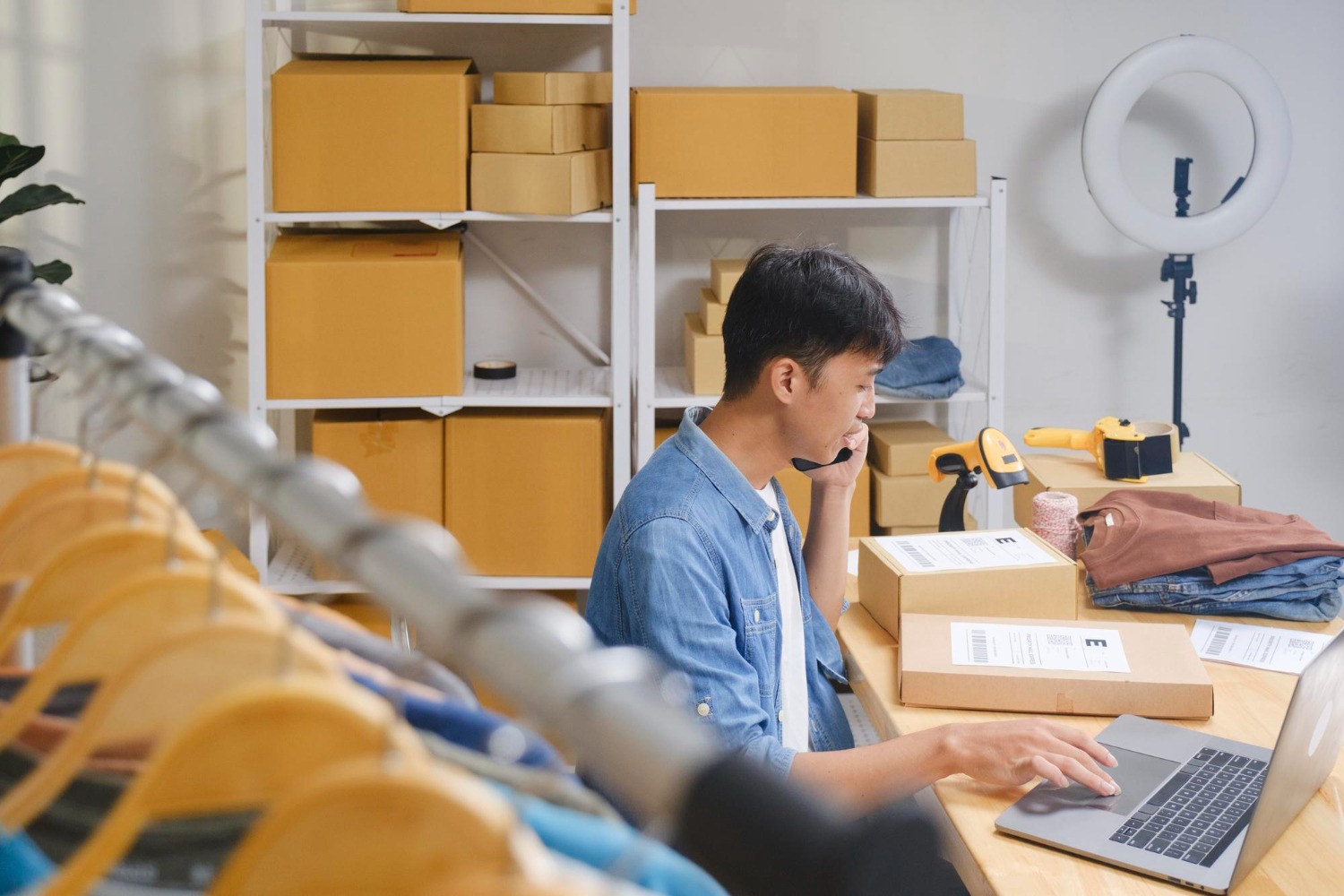 Alt text: Small e-commerce business owner packing and managing online orders at a workstation, using a laptop in a home fulfilment space.