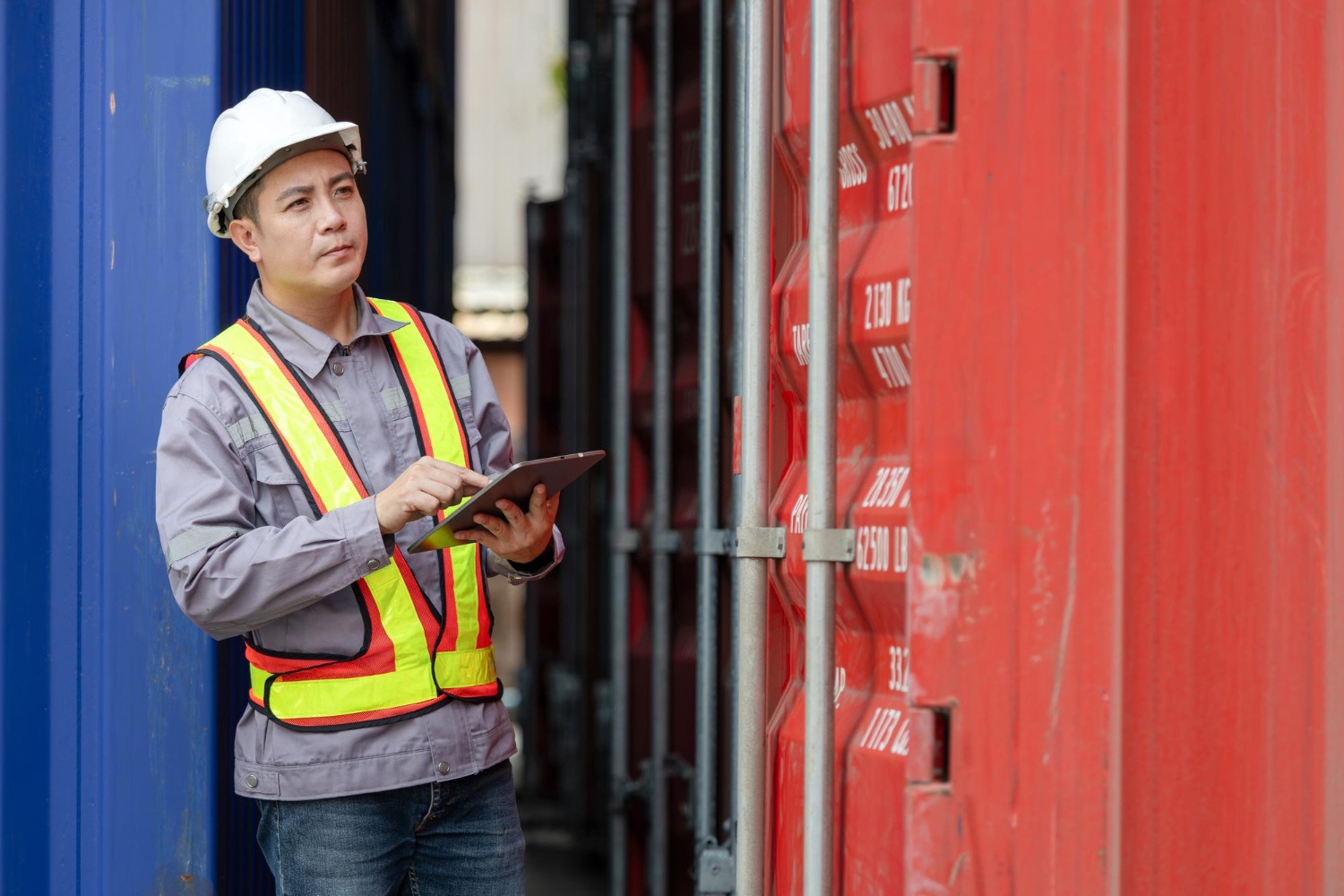 Alt text: Logistics worker inspecting shipping containers with a tablet at a freight terminal.