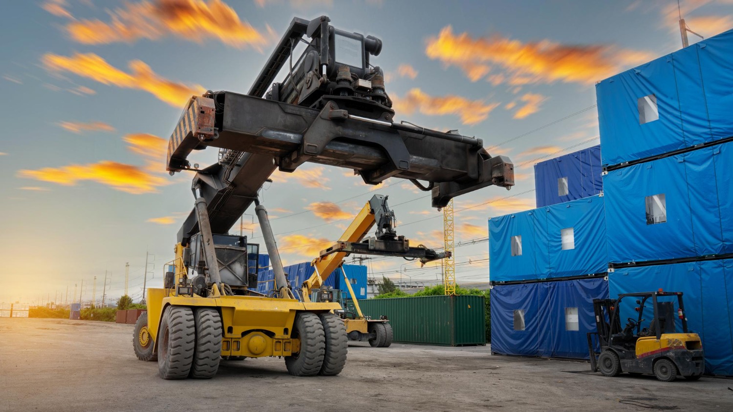 Alt text: Reach stacker handling oversized cargo containers at an industrial freight terminal.