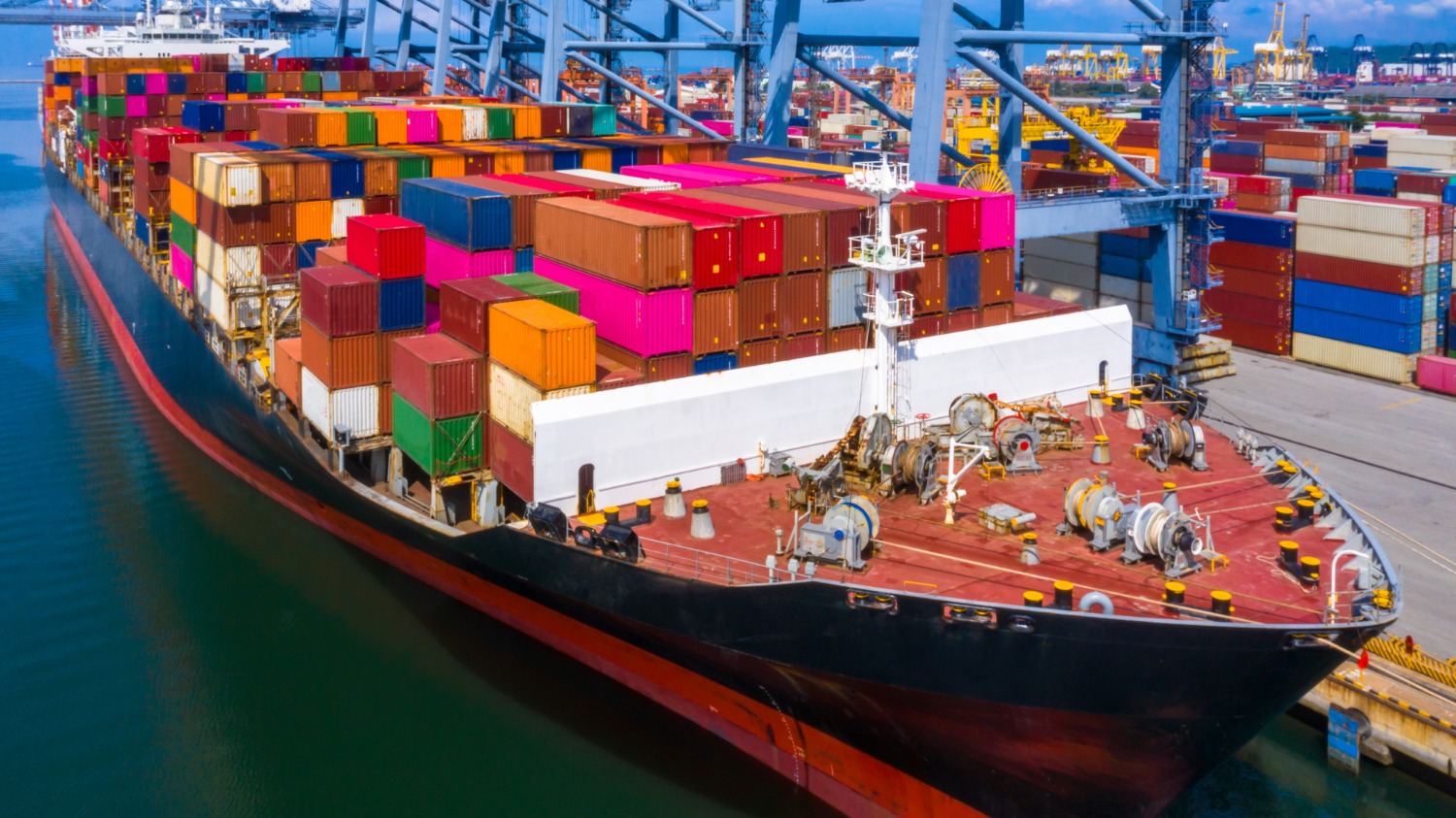 Alt text: Container ship loaded with shipping containers berthed at a busy seaport terminal.