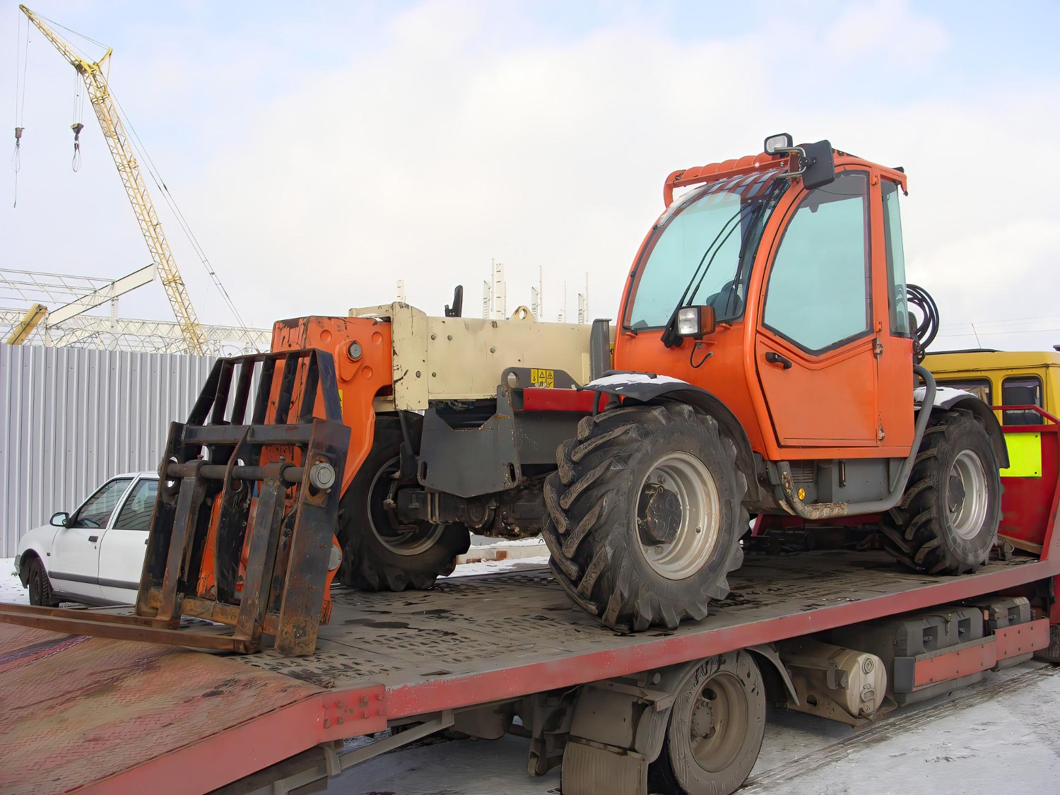 Alt text: Telehandler secured on a flatbed truck for heavy machinery transport at an industrial site.