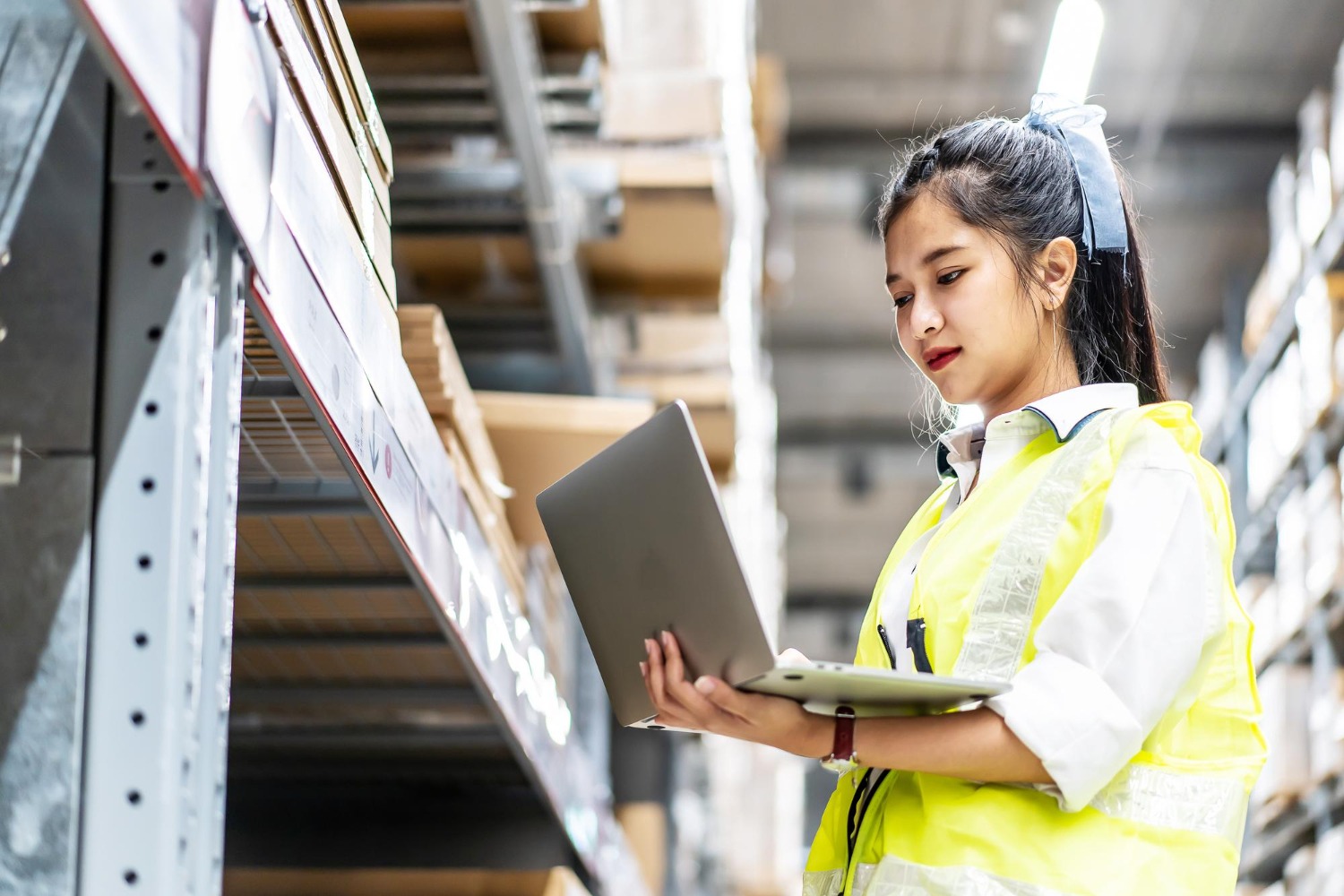 Alt text: Warehouse worker using a laptop to check inventory on storage shelves in an electronics fulfilment warehouse.