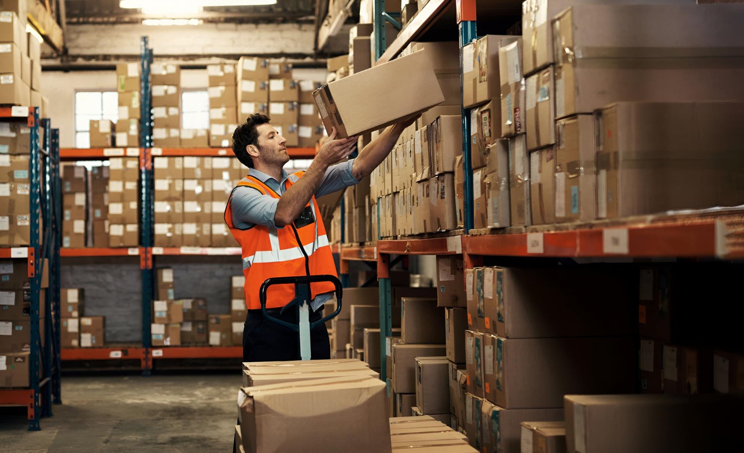 Alt text: Warehouse worker picking a box from storage shelves in a warehouse.