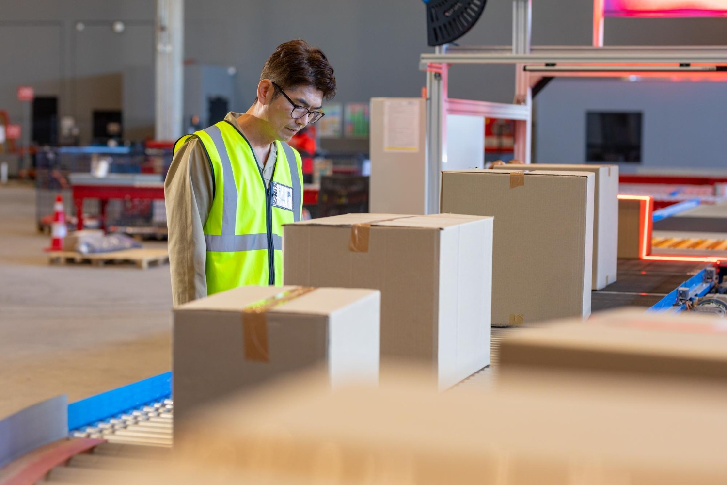 Alt text: Warehouse worker inspecting packed cartons on a conveyor belt at a 3PL fulfilment centre.