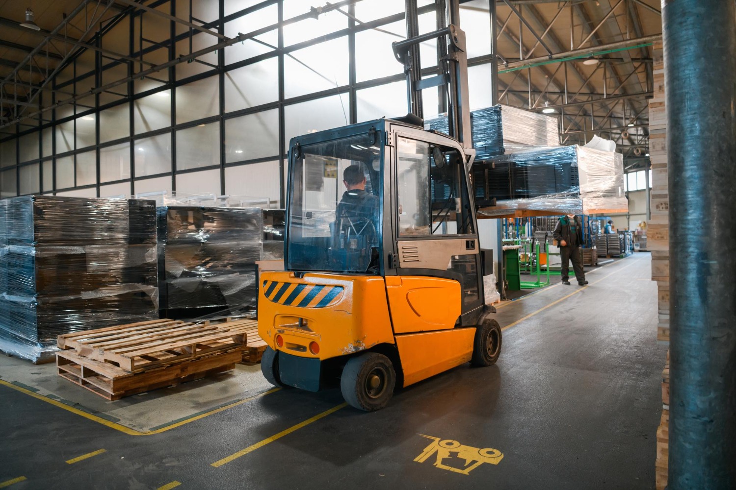 Alt text: Forklift carrying a wrapped pallet through a warehouse with stacked freight ready for shipment.