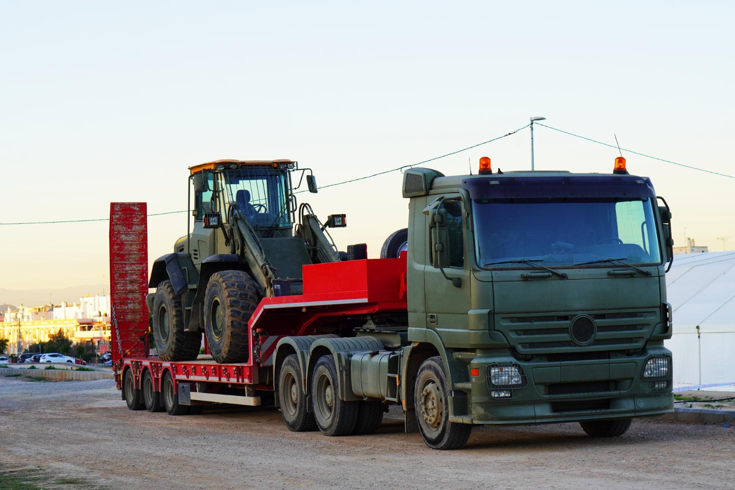 Alt text: Heavy agricultural loader transported on a low-loader truck for freight and import logistics