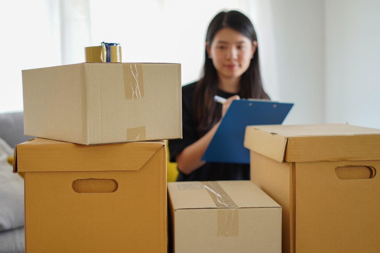 Alt text: Person checking a moving checklist beside packed cardboard boxes before relocating to New Zealand.