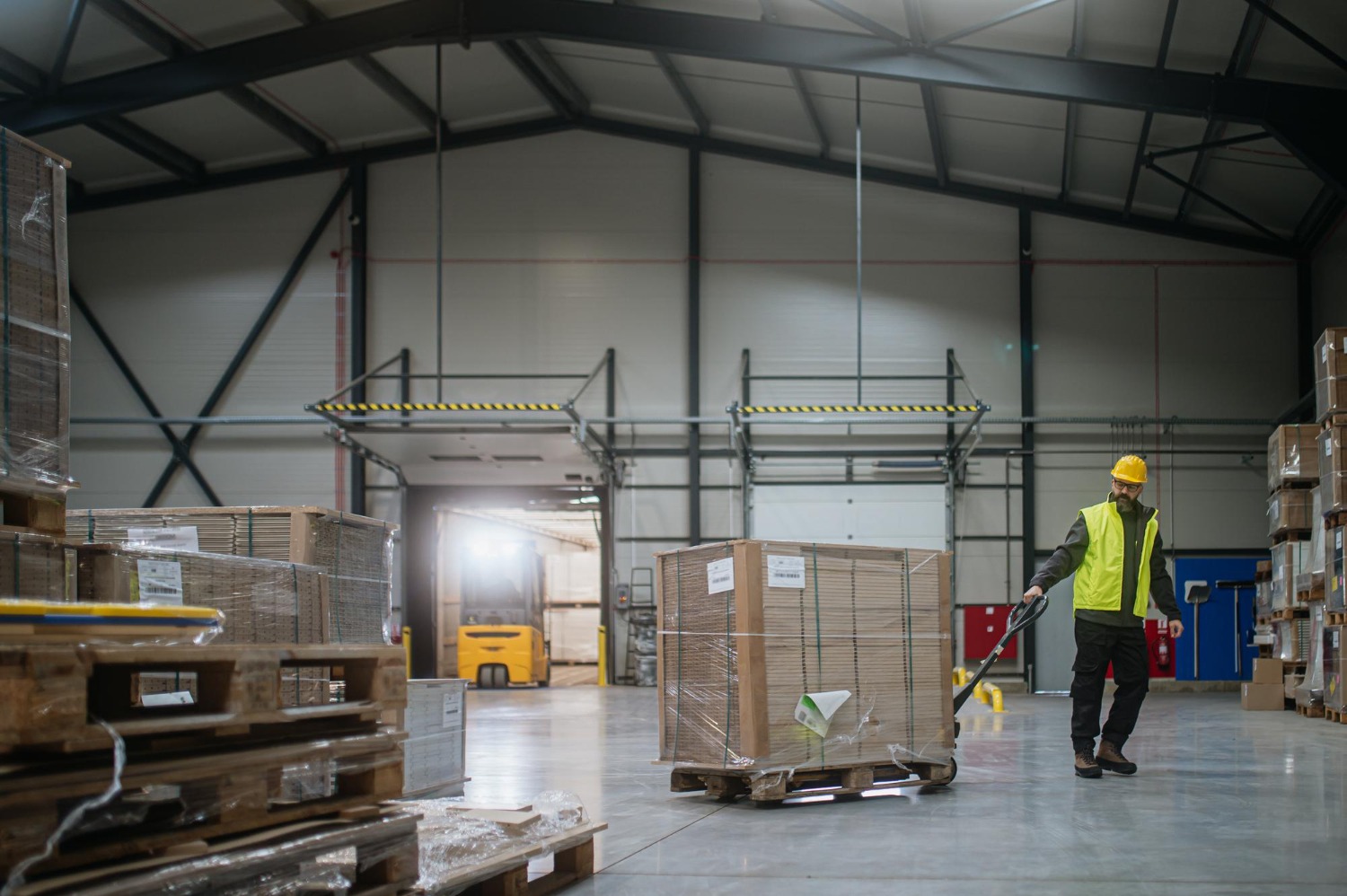 Alt text: Warehouse worker maneuvering pallet jack loaded with goods through warehouse.