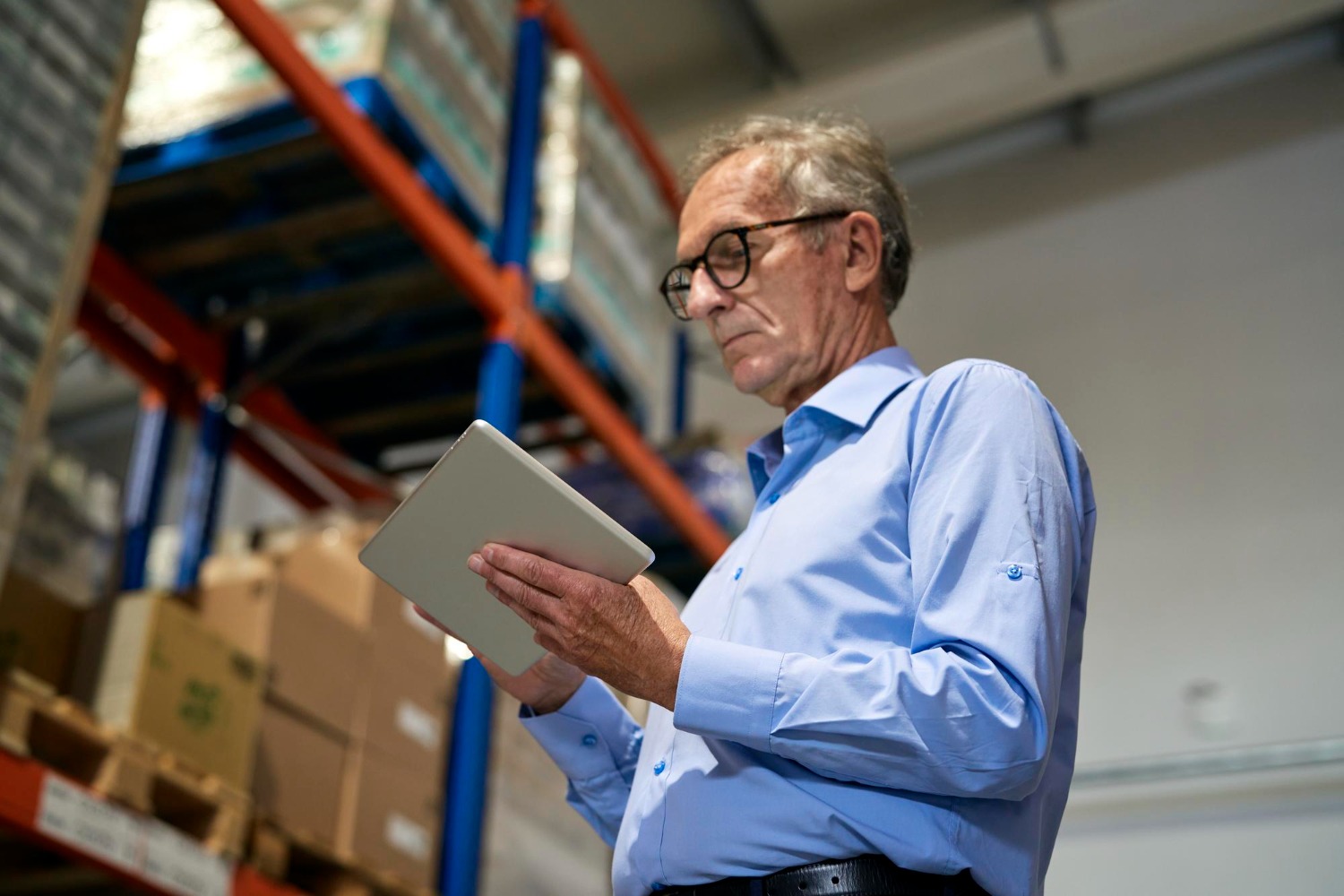 Alt text: Warehouse worker using a tablet while inspecting stock in a warehouse.