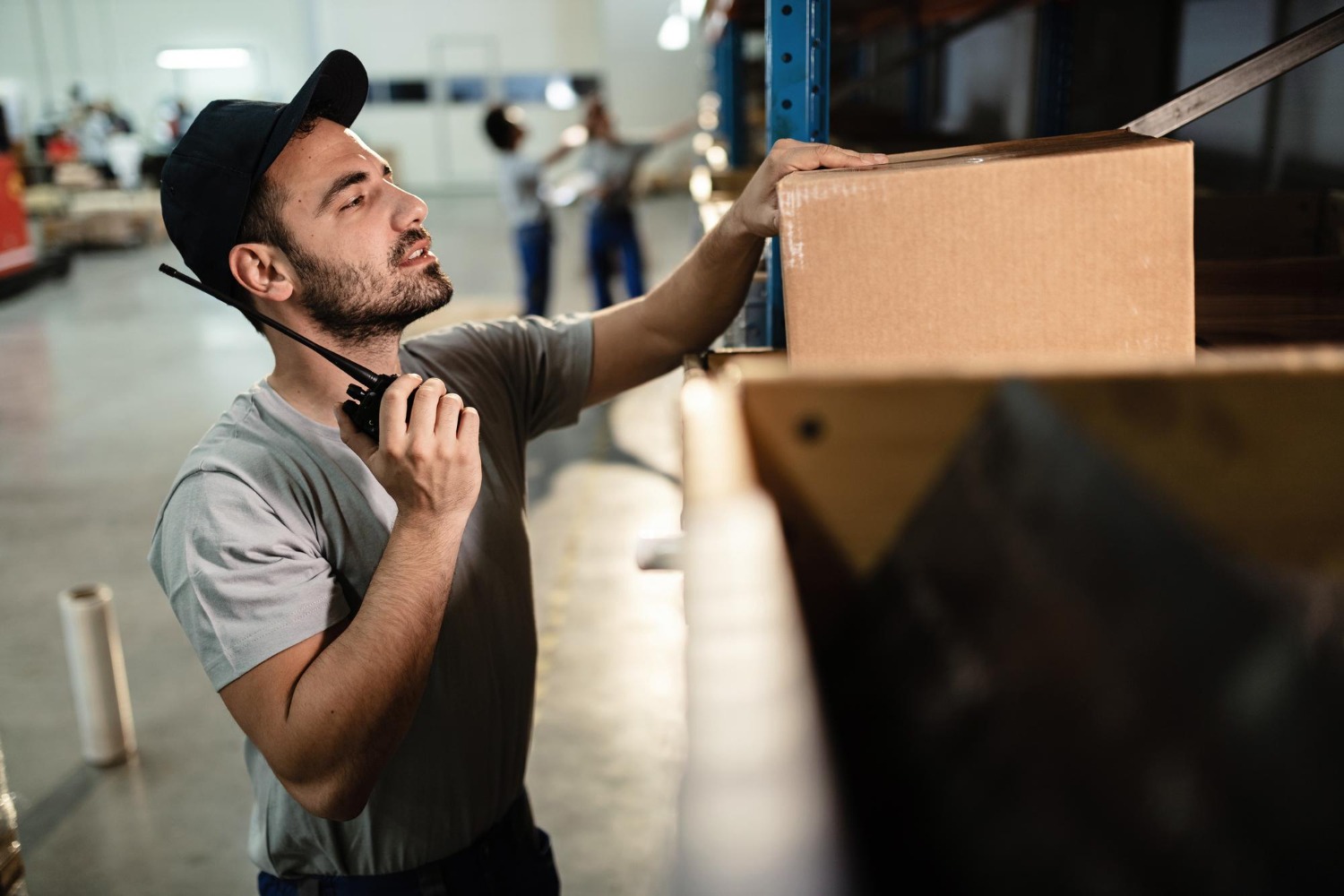 Alt text: Warehouse worker checking a cardboard box on a storage shelf.