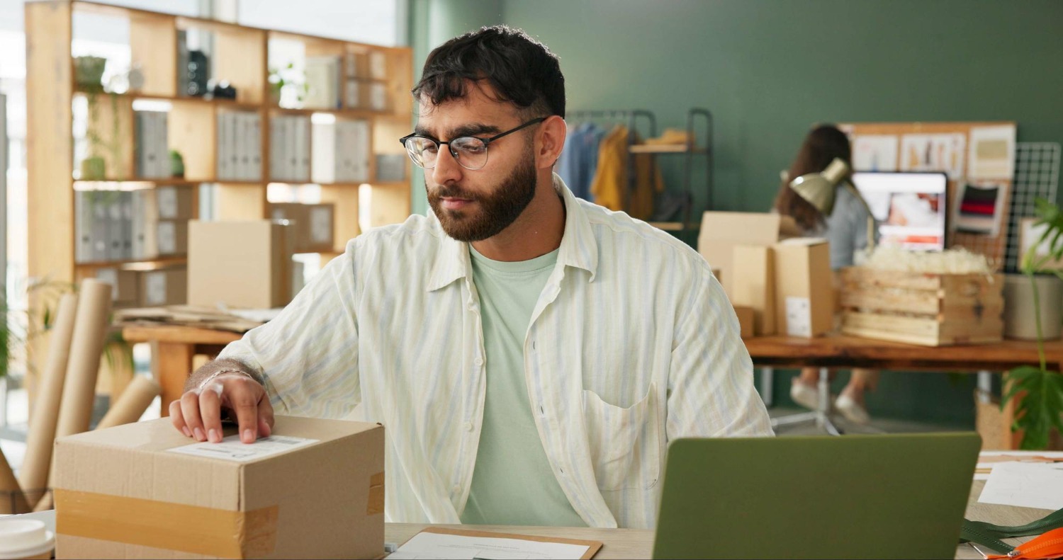 Alt text: A business owner preparing an international parcel with shipping documents and a laptop.